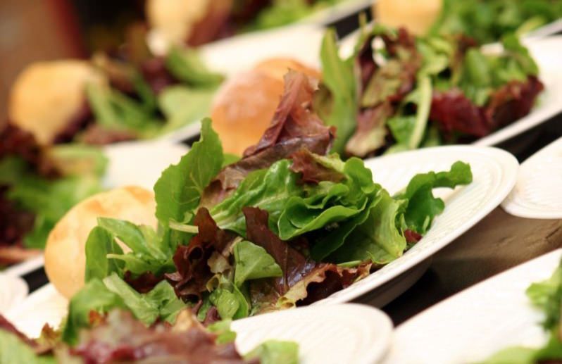 Plates of fresh mixed green salad with leafy greens and tomatoes on a table