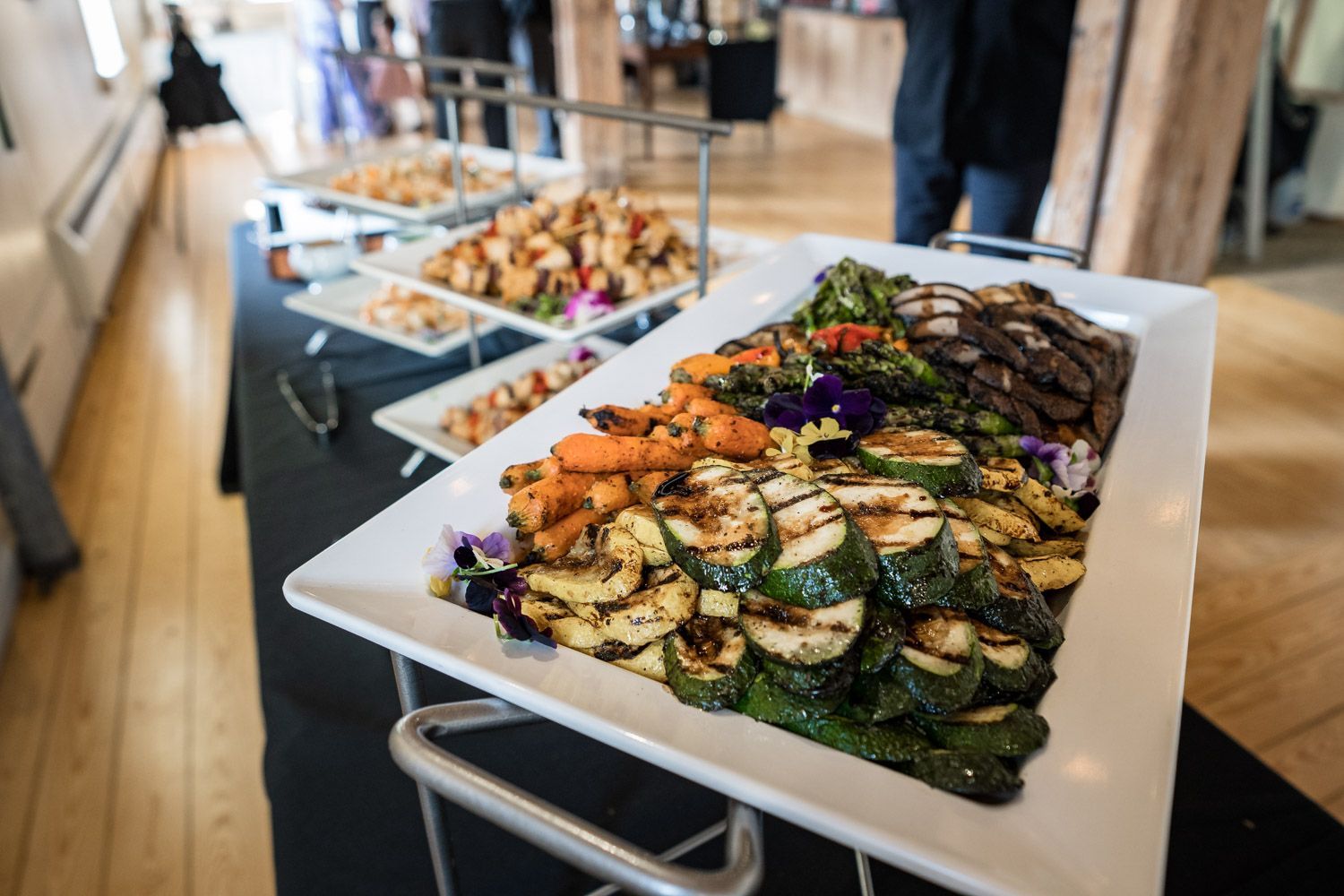 Buffet table with trays of roasted vegetables, salad, and assorted dishes in a dining hall