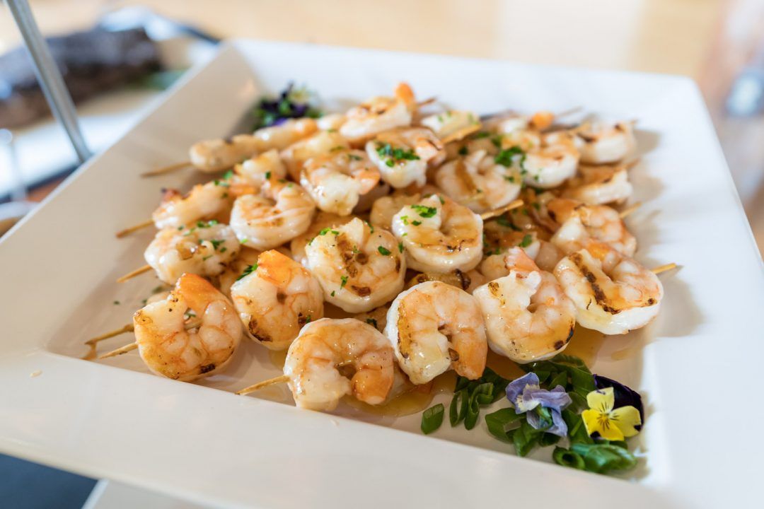 Plated shrimp appetizer garnished with herbs and flower petals on a white square dish