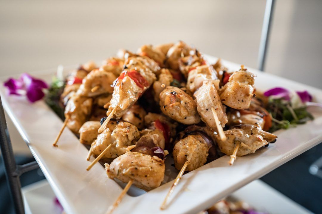 Skewered grilled chicken bites on a white platter, garnished with herbs and purple flowers