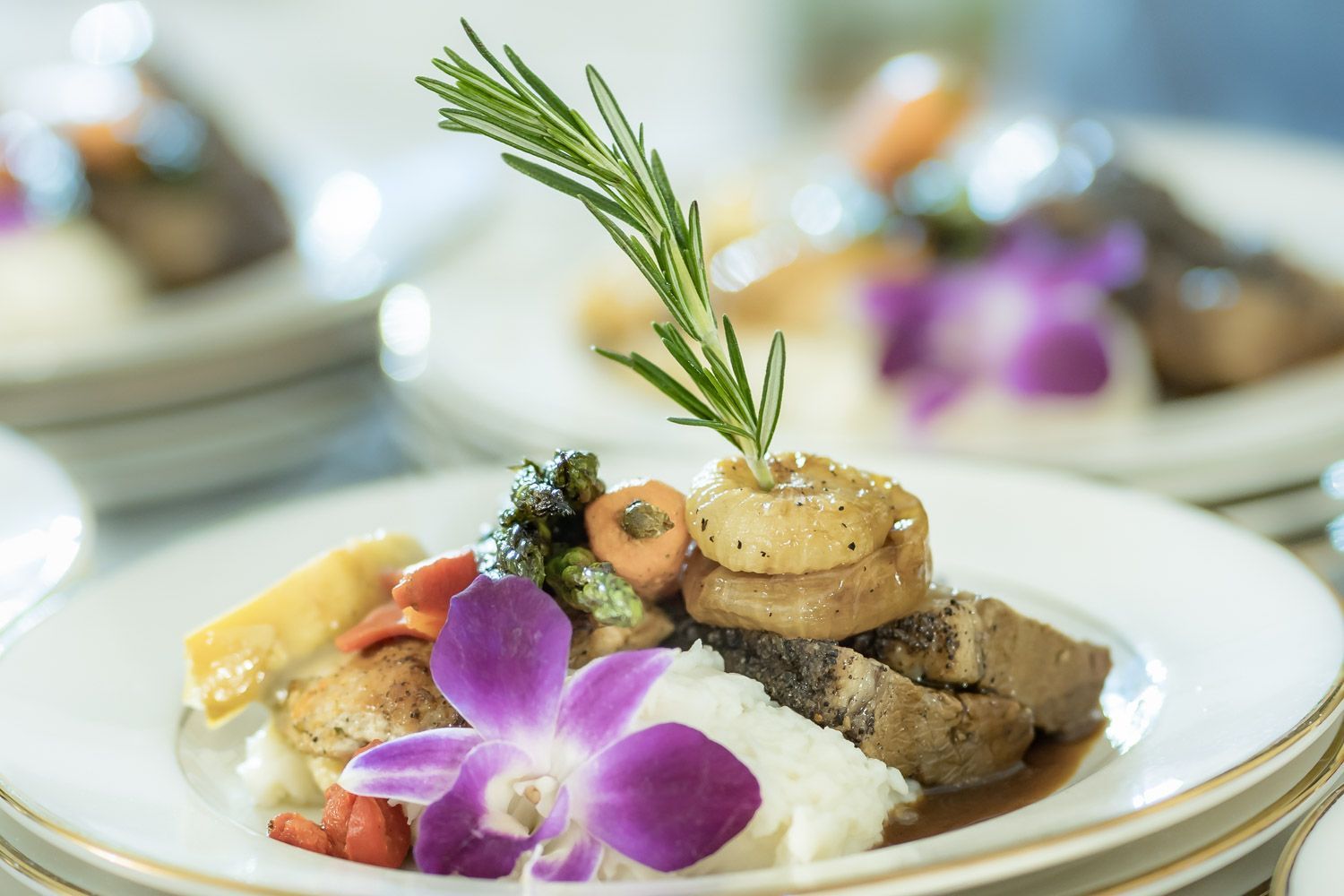 Gourmet plated entrée with roast meat, sauce, potatoes, and purple orchid garnish on a white plate