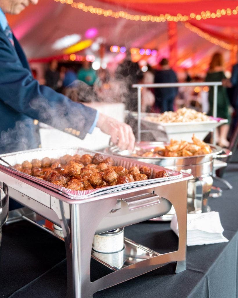 Catered buffet with trays of fried snacks under a red tent, a person serving food at the left.