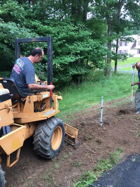 a man is driving a tractor next to a man digging in the dirt .