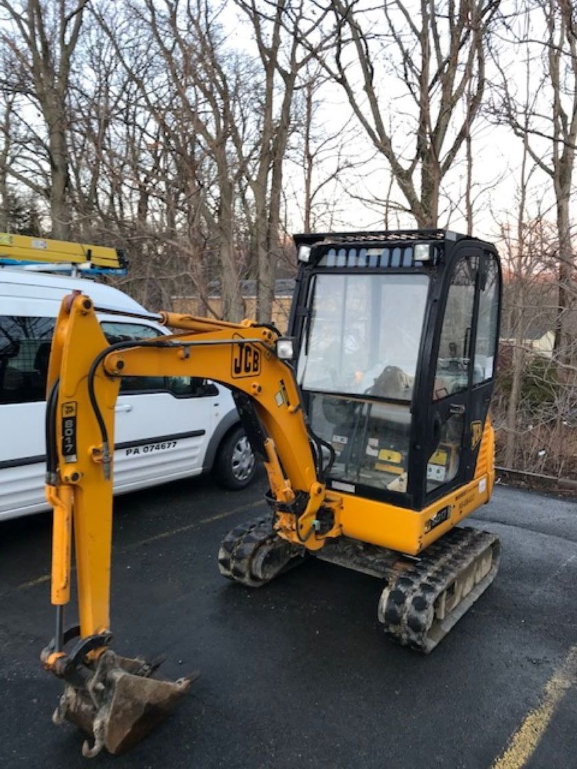a small yellow excavator is parked in a parking lot next to a white van .