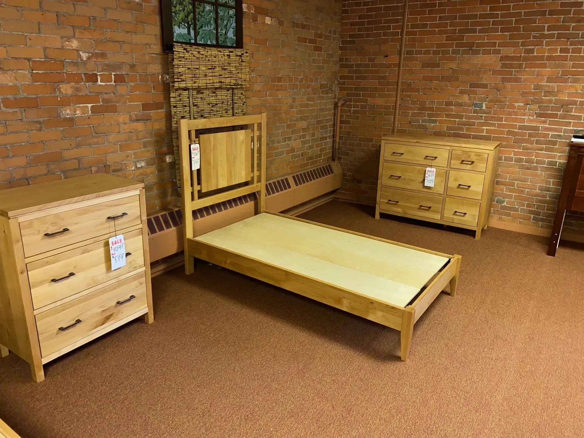 Bedroom furniture set: Light wood bed frame, two dressers, brick wall background.