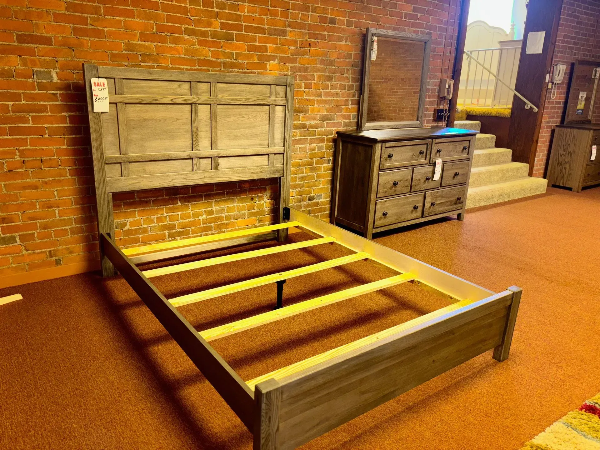 Wooden bed frame with headboard, dresser, and mirror in a brick-walled store.