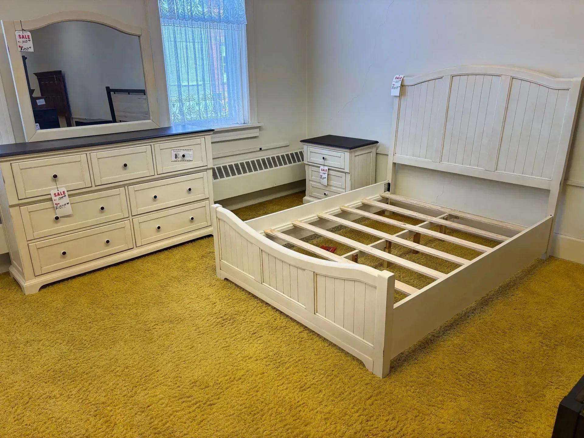 Bedroom furniture set: bed frame, dresser with mirror, nightstand; cream color with dark brown top on the dresser.