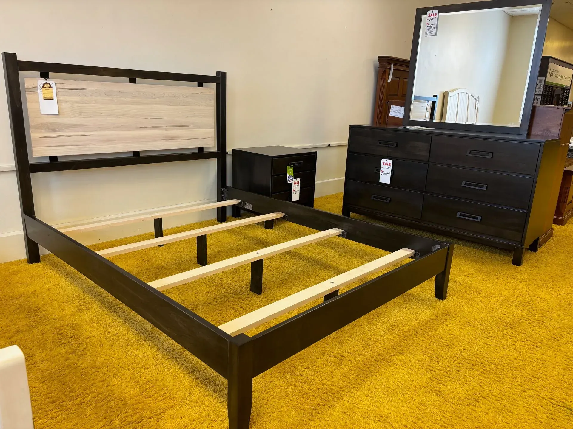 Bedroom furniture set: black bed frame with wood headboard, dresser, nightstand, and mirror on yellow carpet.
