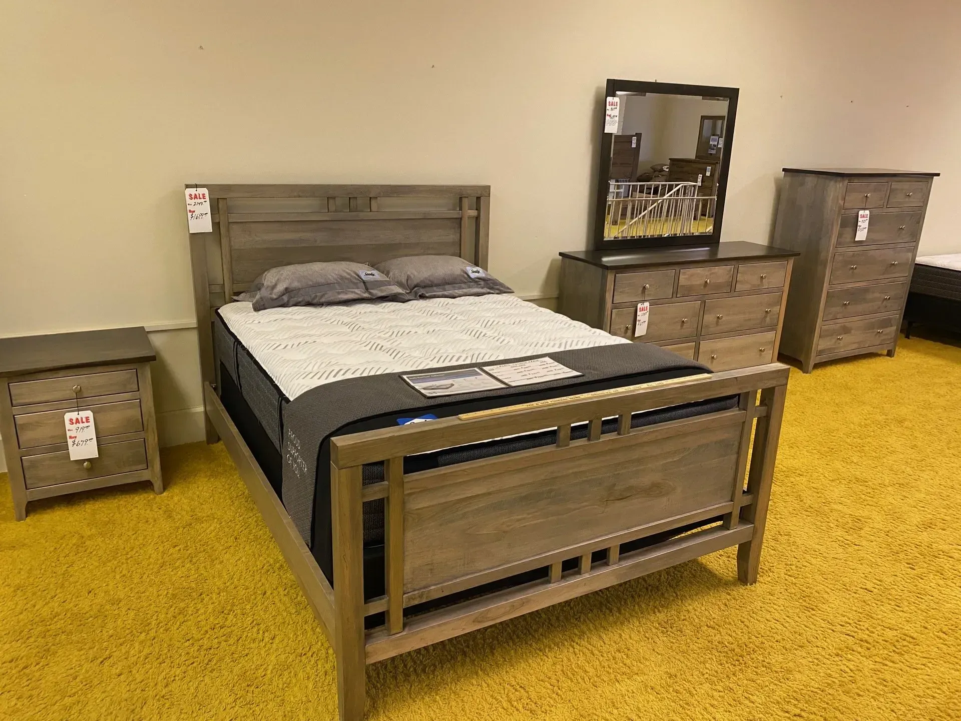 Bedroom set with bed, nightstand, dresser, and mirror in a showroom, all light wood.