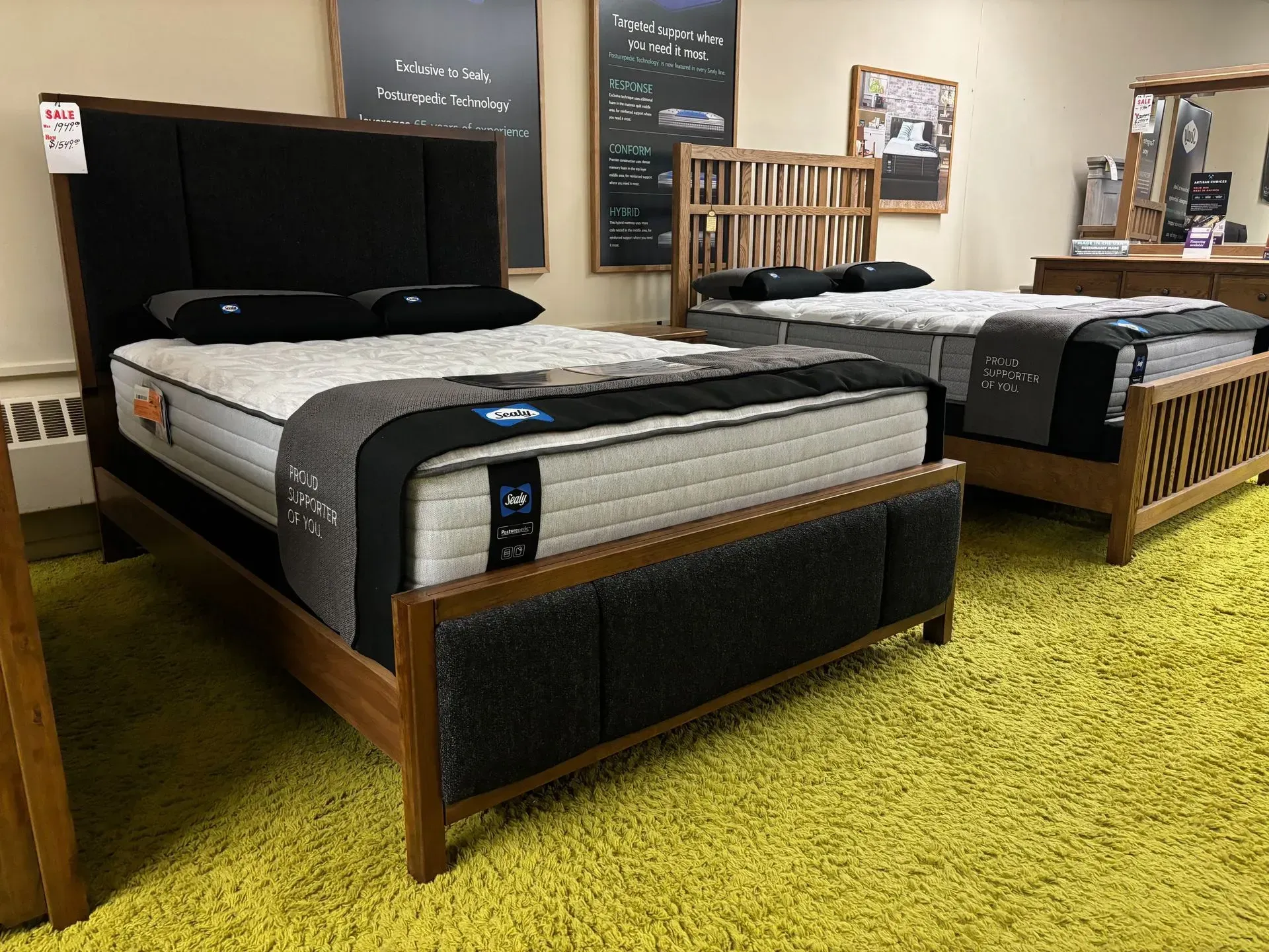 Beds displayed in a furniture store on a green carpet. Dark wood frames, black headboards, mattresses.