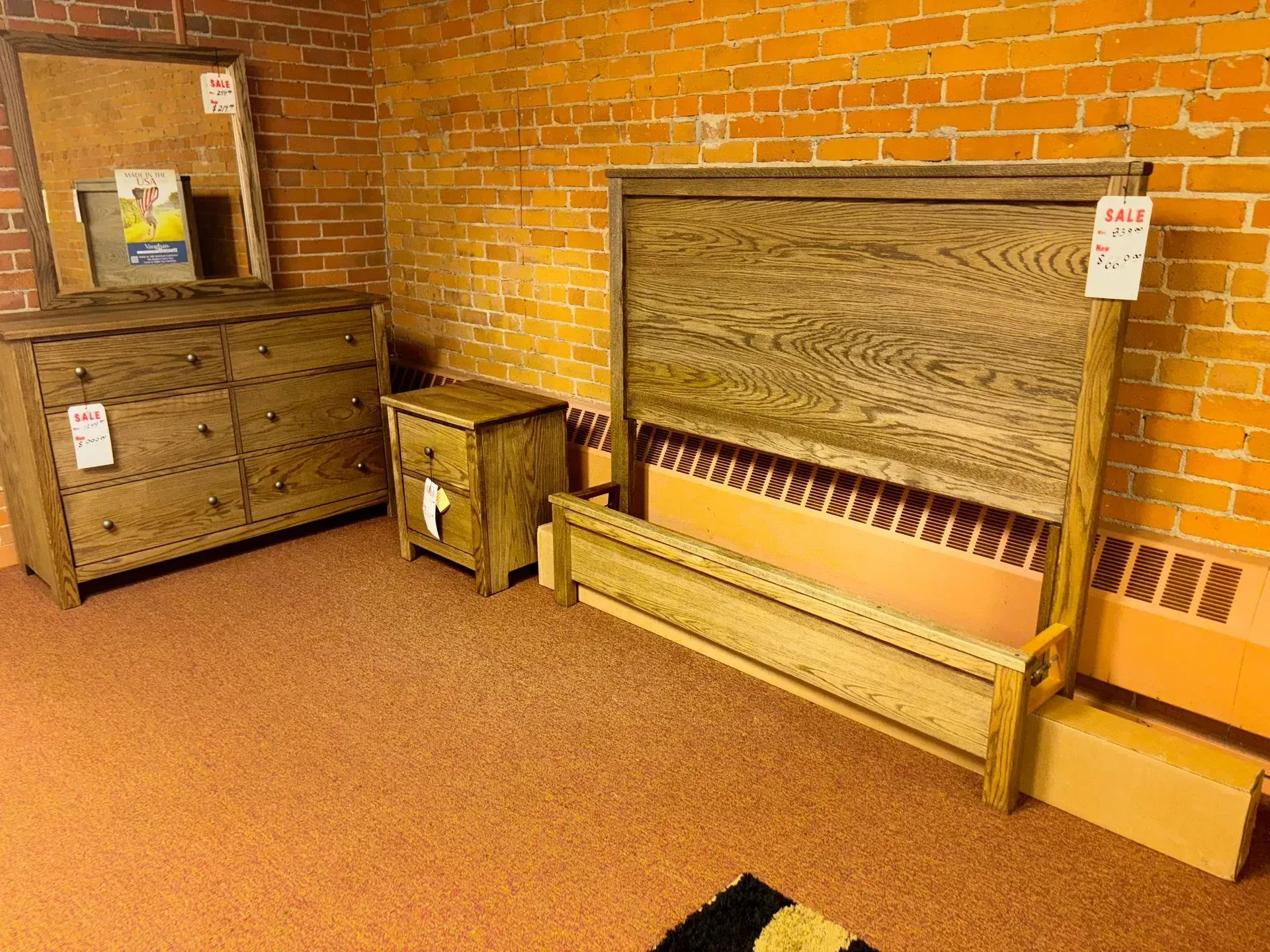 Bedroom furniture set on display against a brick wall: dresser, nightstand, bed frame.