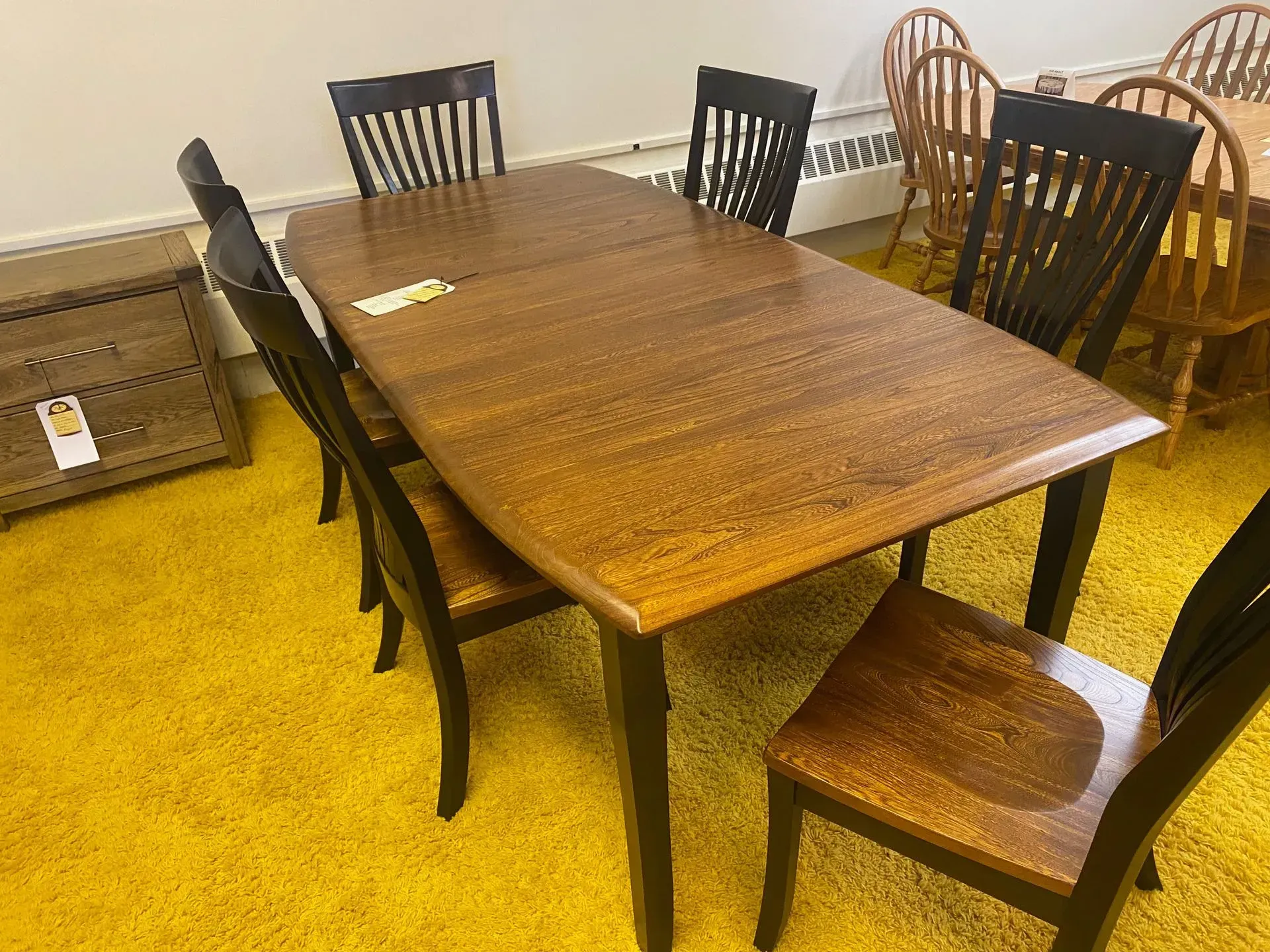Wooden dining table with six chairs on yellow carpet.