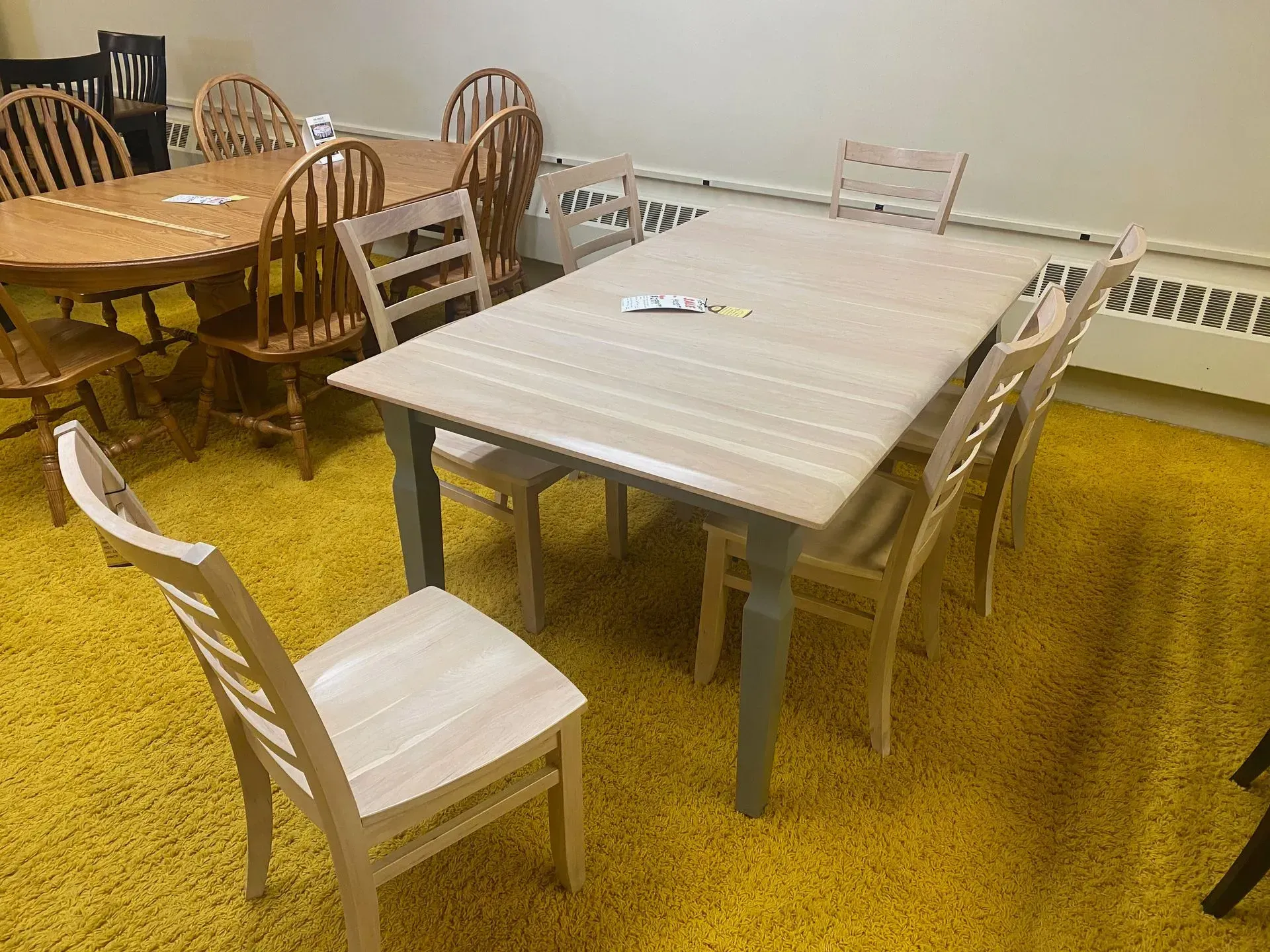 Dining tables and chairs on yellow carpet. A light wooden table with grey legs is the main focus.