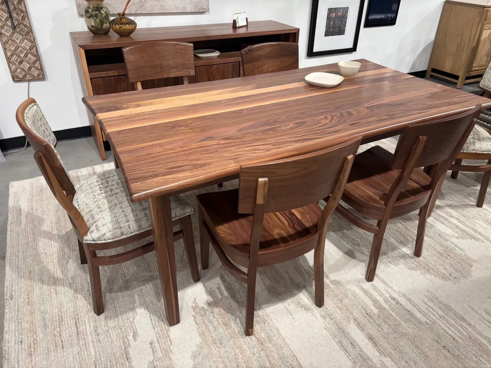 Wooden dining table with six chairs, a buffet, and framed artwork in a furnished room.