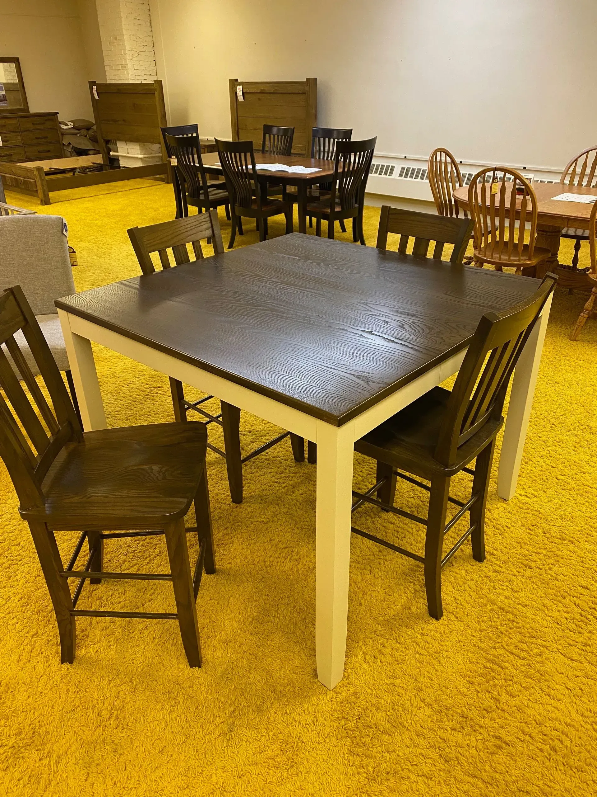 A square dining table with four chairs on a yellow carpet in a furniture store.