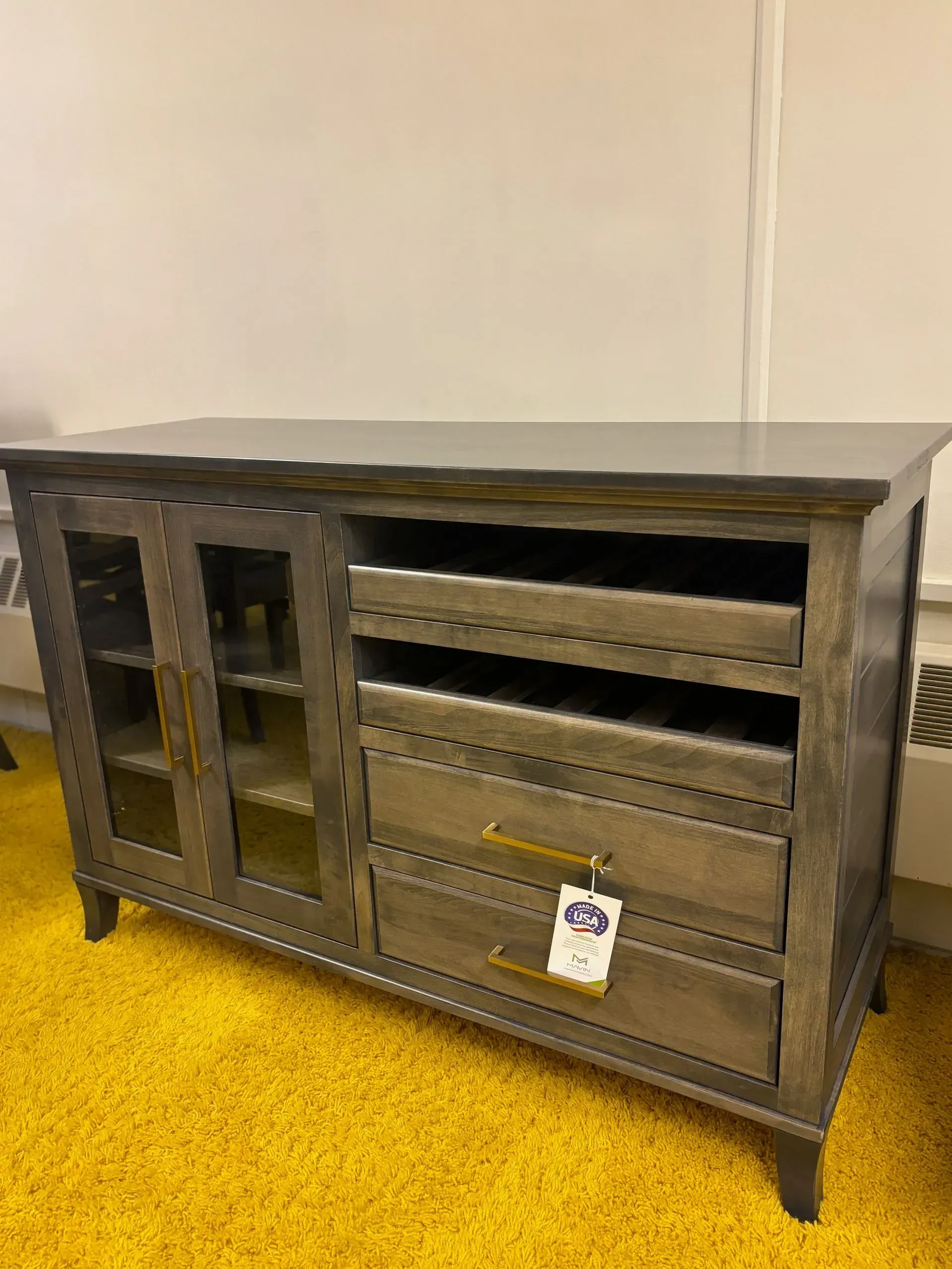 Wooden media console with glass door cabinet, drawers, and open shelving, in a room with a yellow carpet.