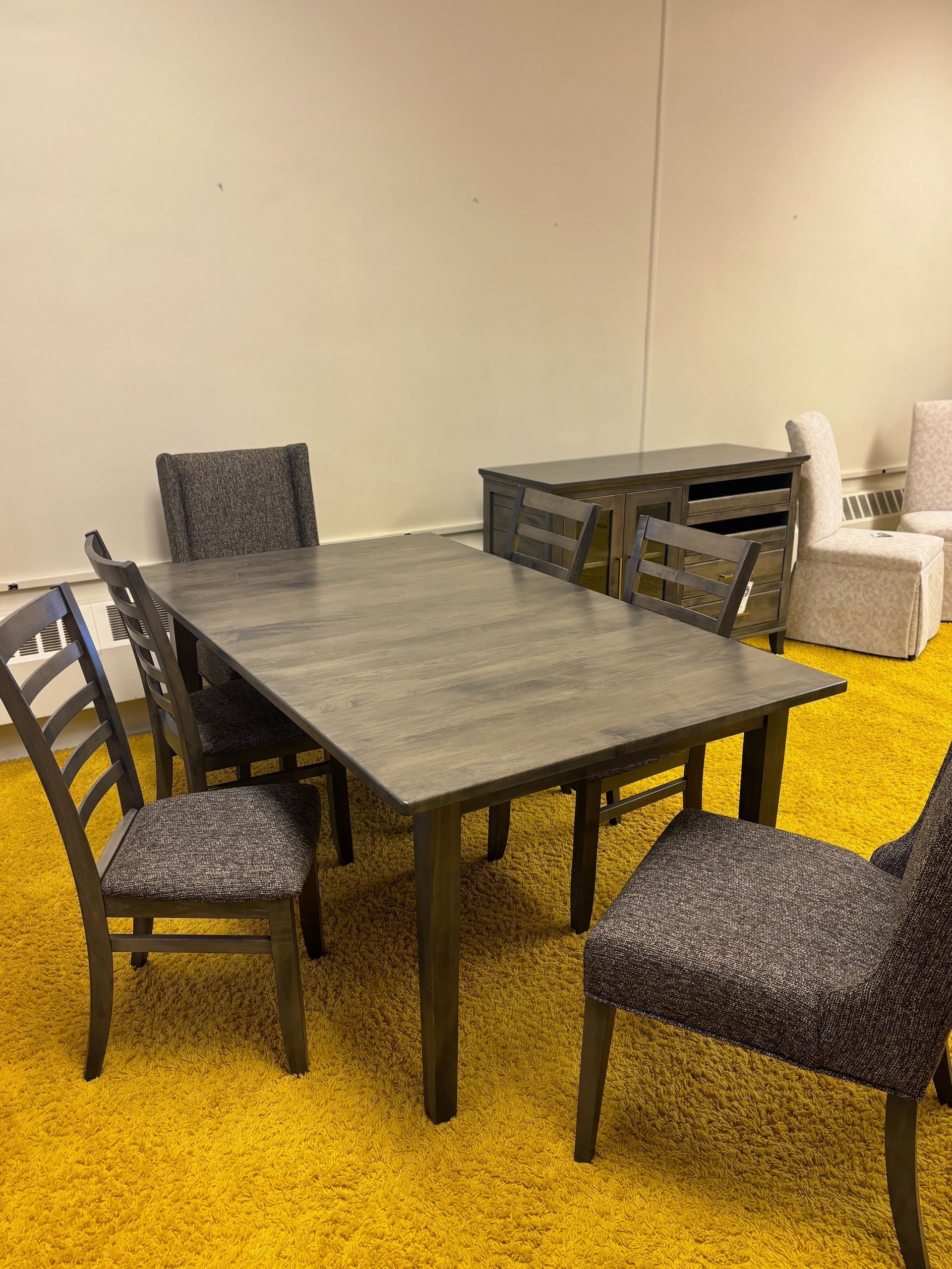 Dining set on yellow carpet: gray table, four patterned chairs, gray buffet, white wall.