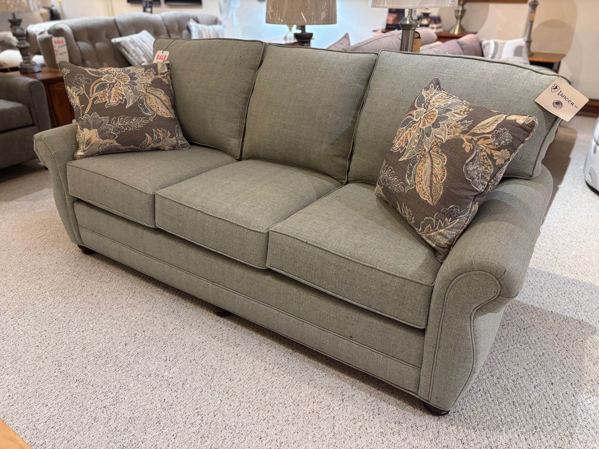 Green upholstered sofa with two patterned throw pillows, displayed in a furniture store.
