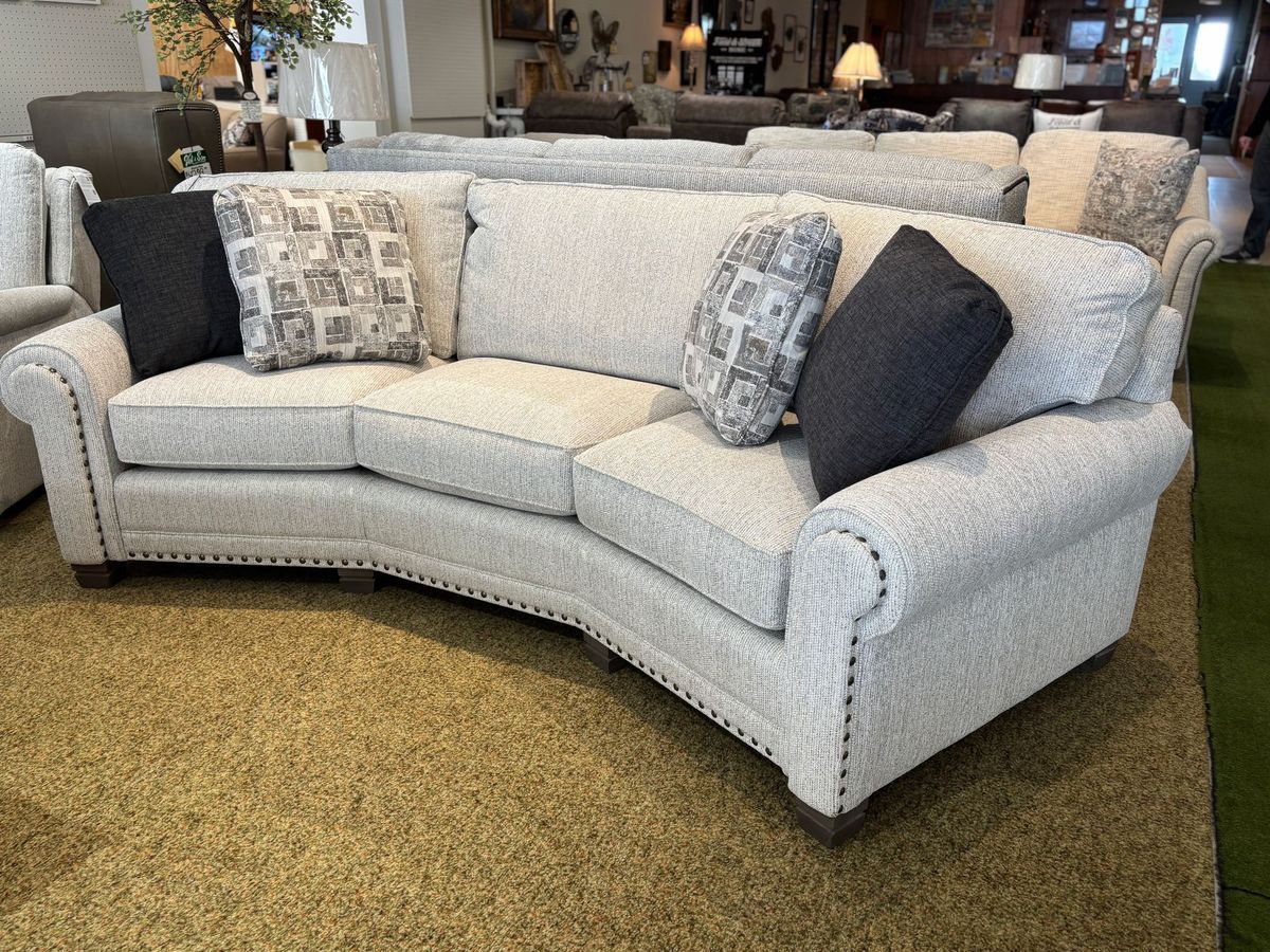 Curved beige sofa with decorative pillows, set on a patterned rug, in a furniture store.