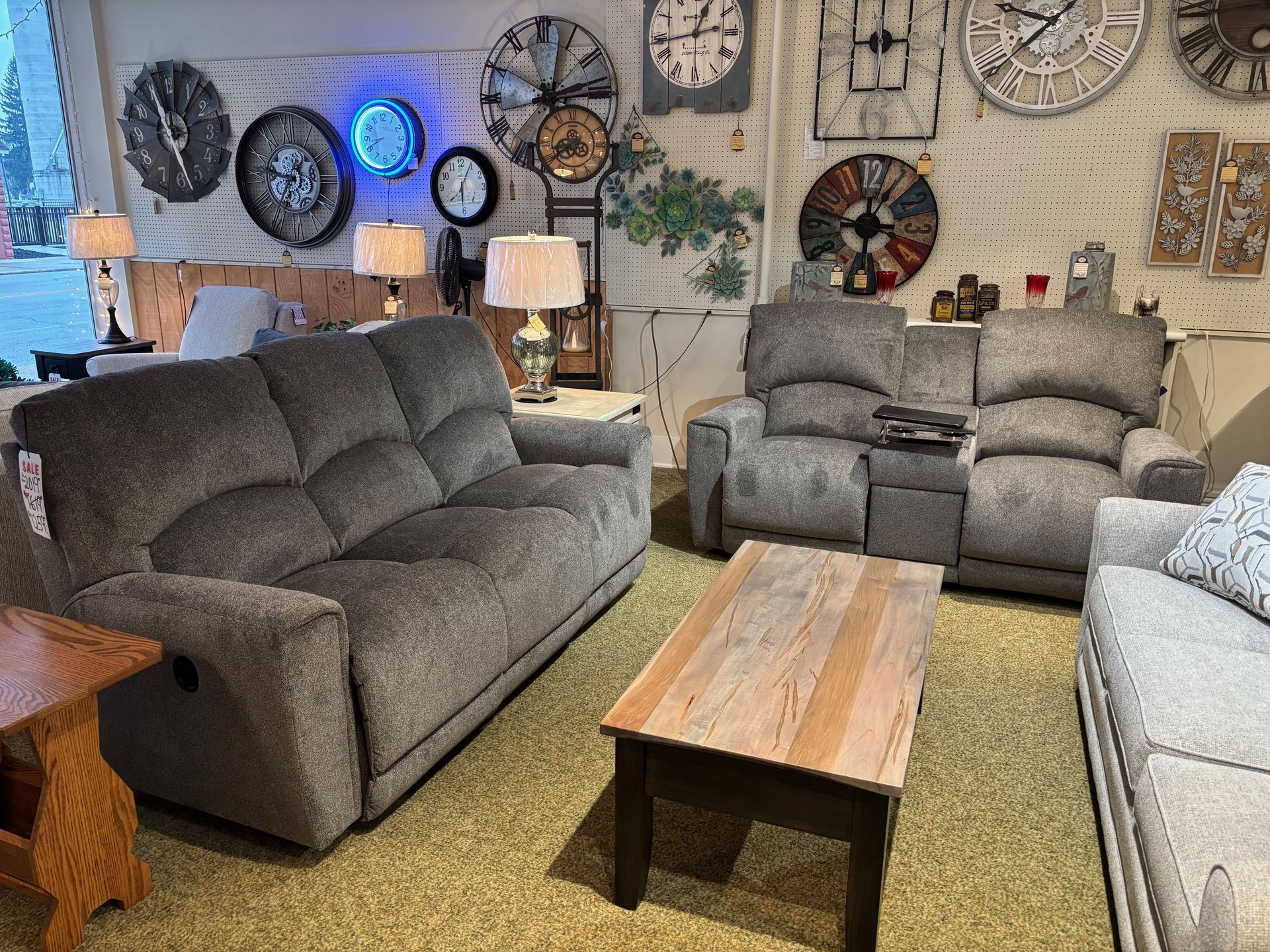 Gray reclining sofa and loveseat in a furniture showroom with coffee table, clocks, and lamps.
