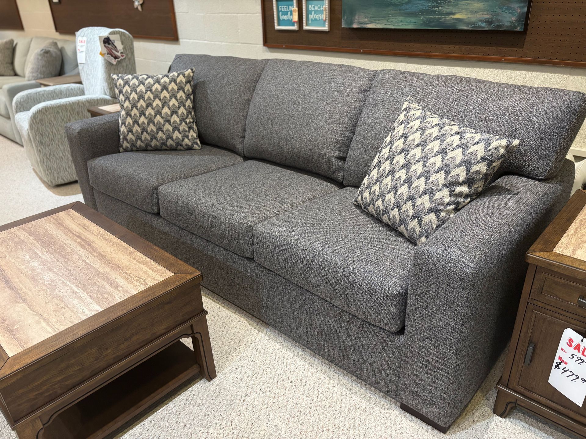 Gray fabric sofa with patterned pillows, wood side tables in a furniture store.