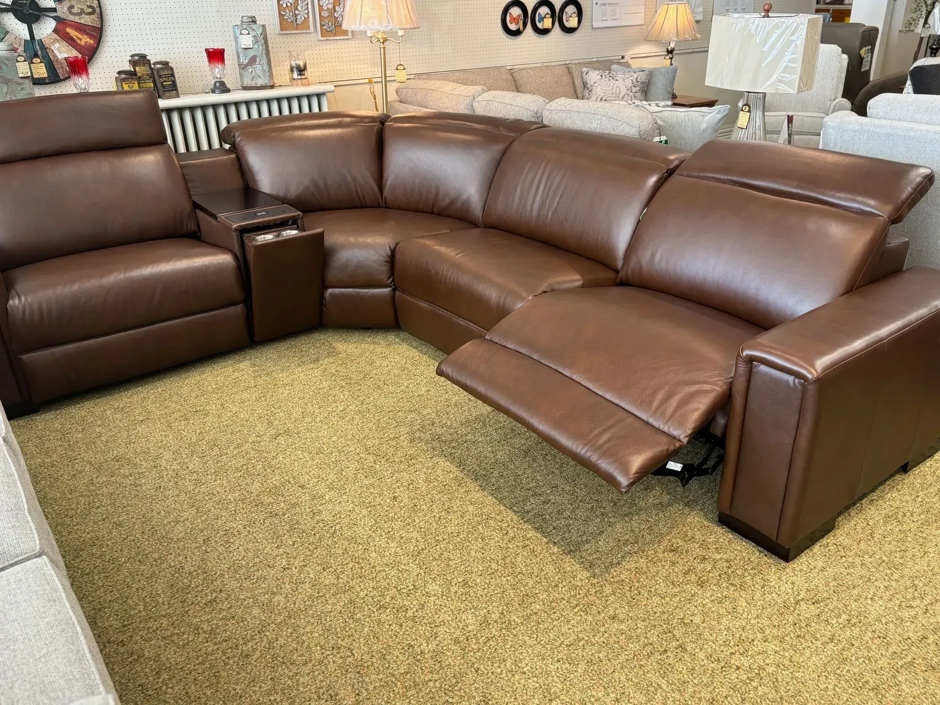 Brown leather sectional sofa with reclined seats and built-in cup holders on tan carpet.