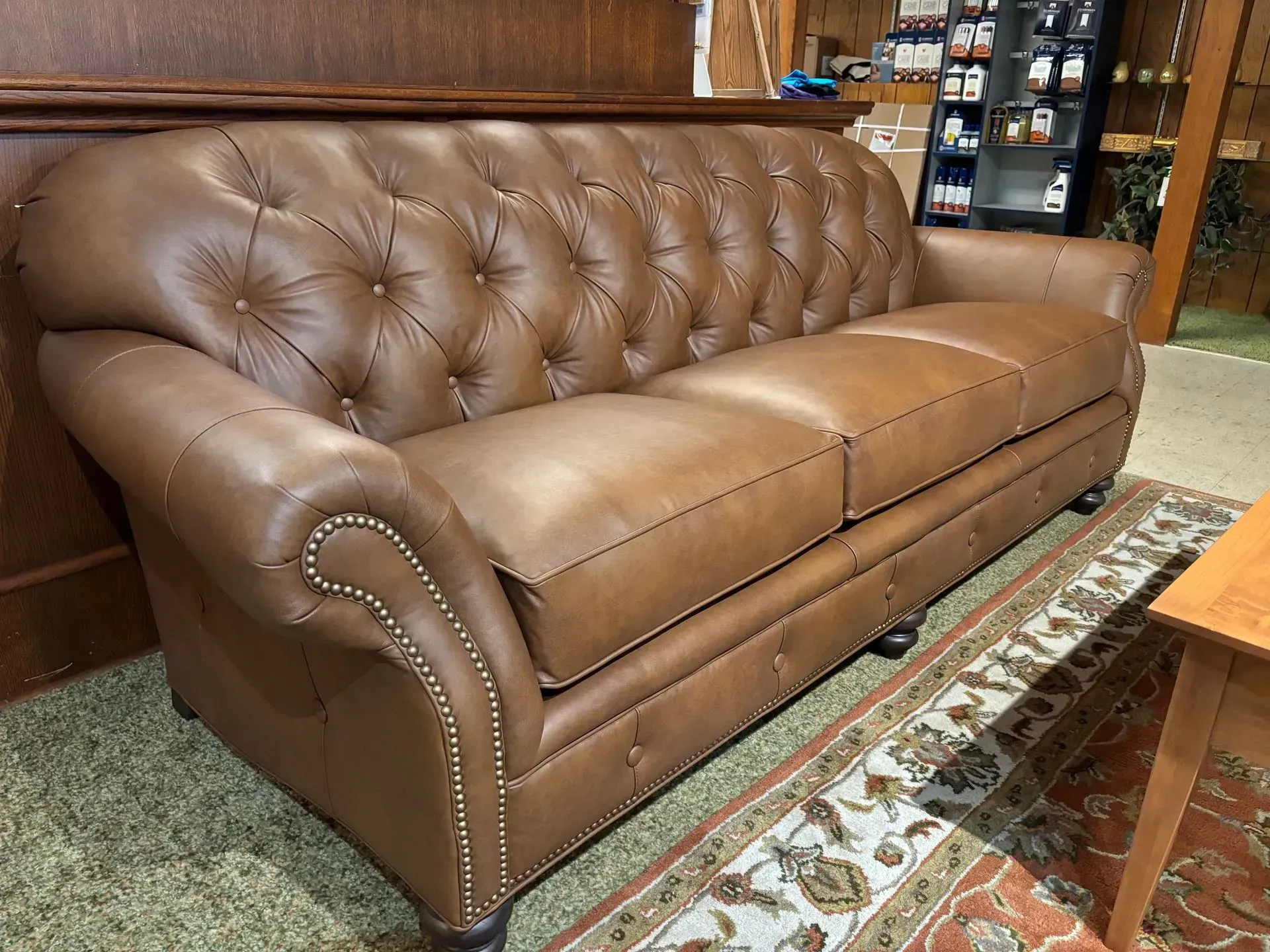 Brown leather tufted sofa with nailhead trim, indoors on patterned rug.