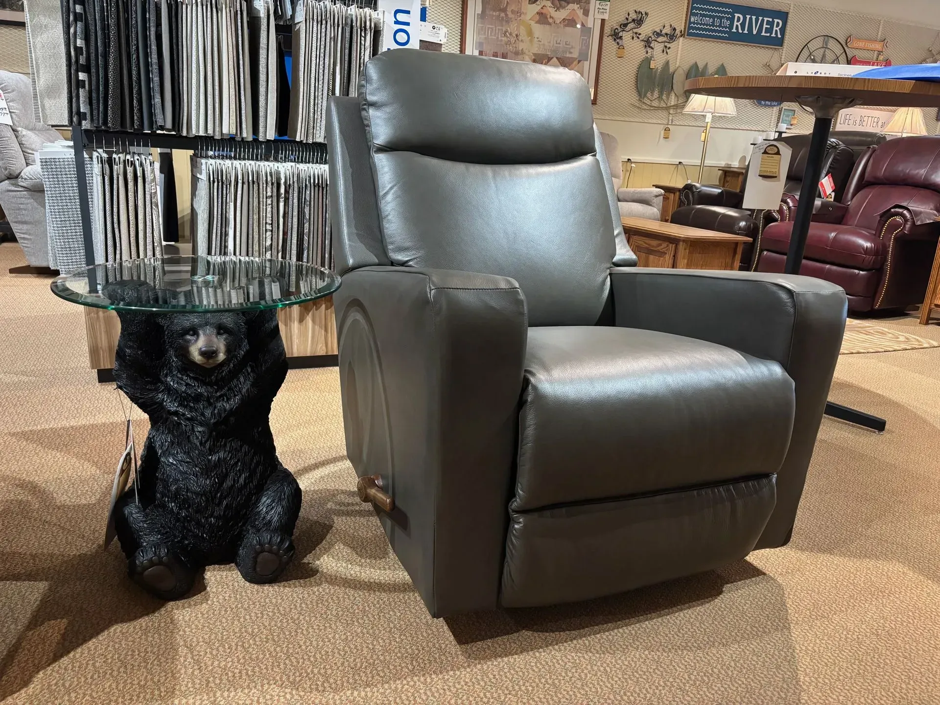 Gray leather recliner next to a bear-shaped side table with a glass top in a furniture store.