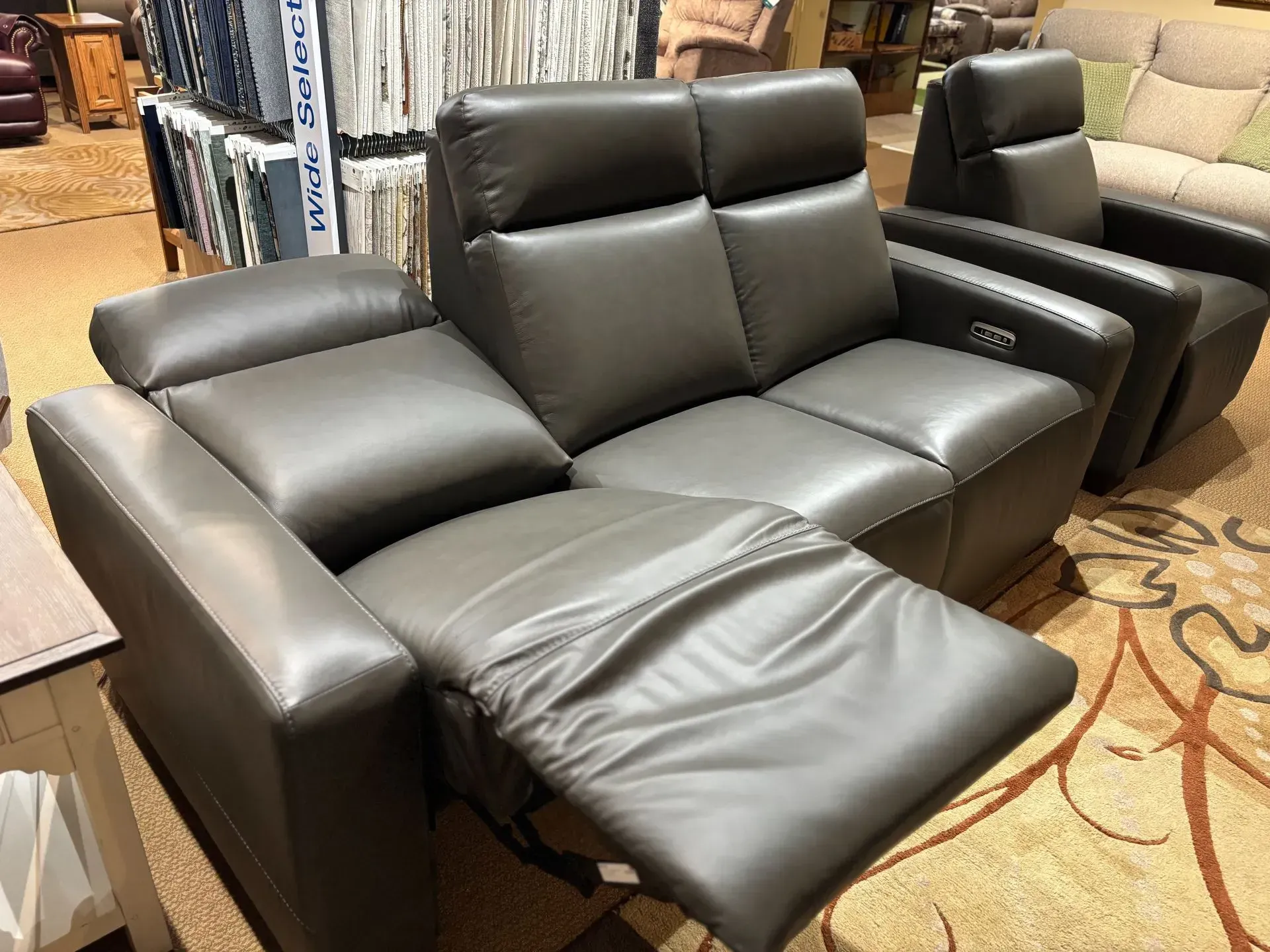 Gray leather reclining loveseat with one reclined seat in a furniture store.