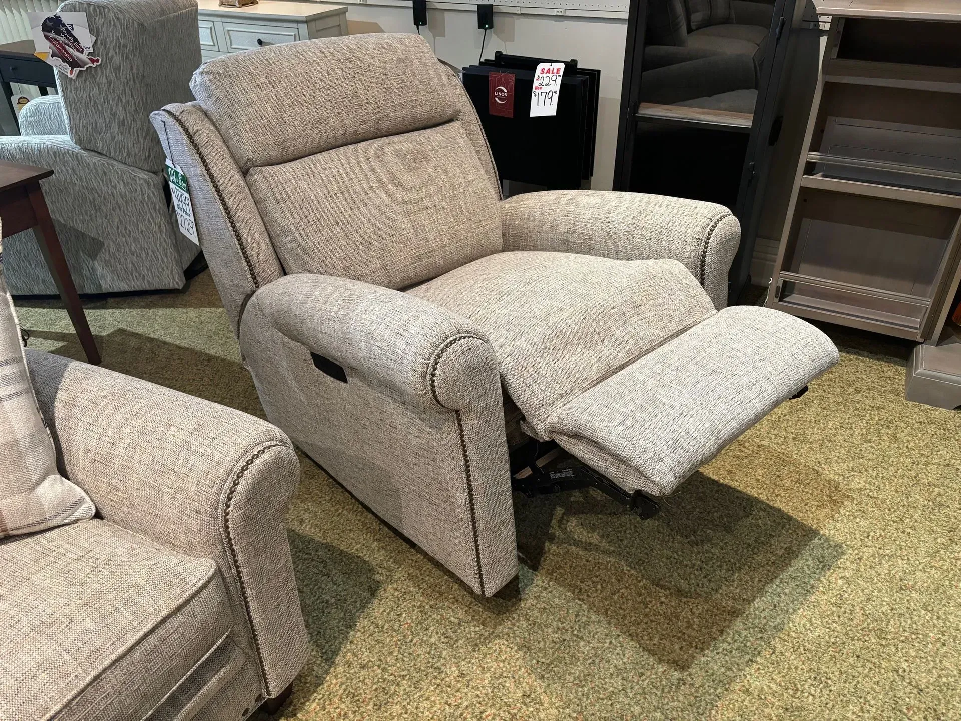 Beige recliner with footrest extended, in a furniture store setting.