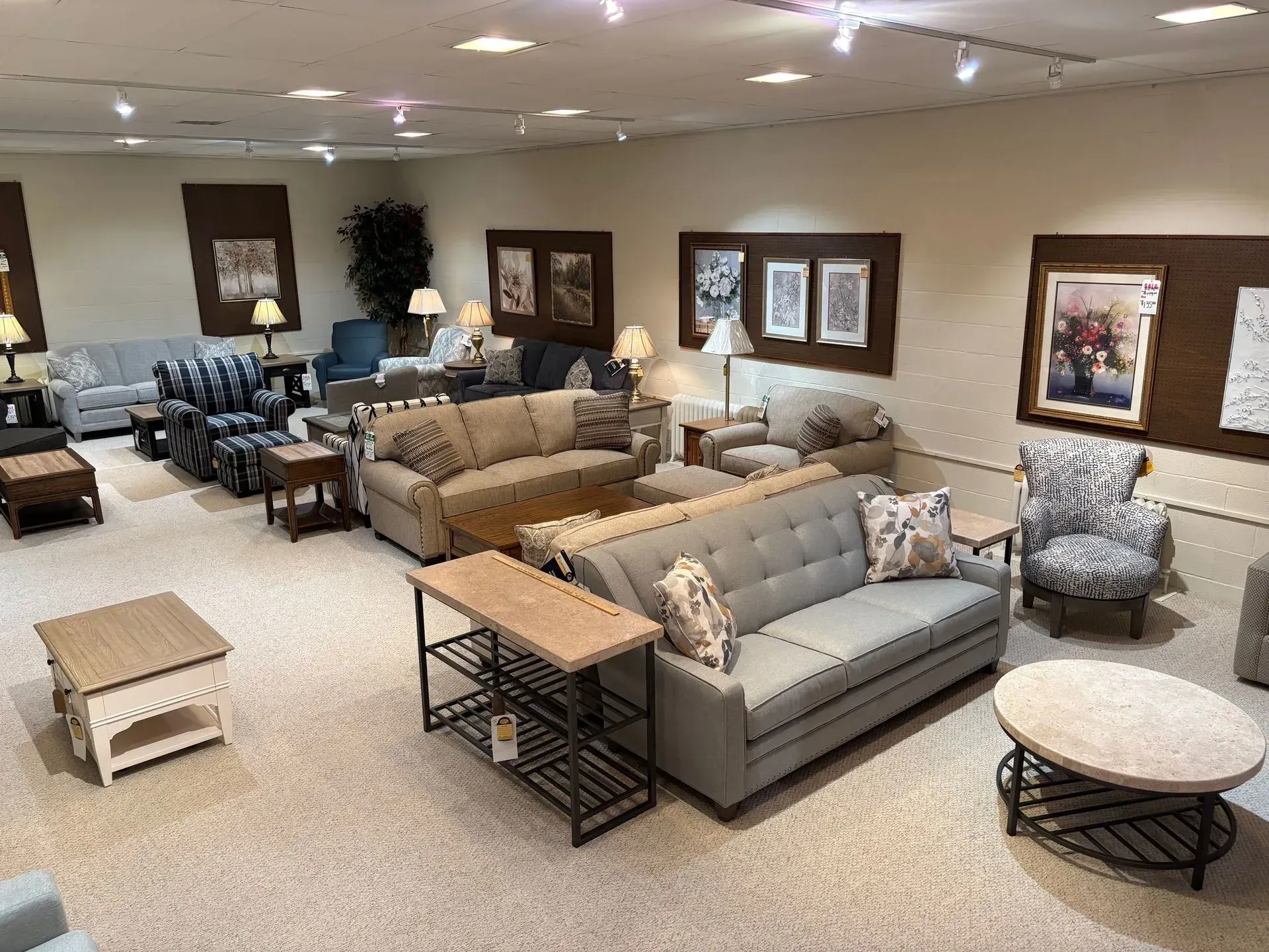 Furniture store showroom with various couches, chairs, and tables on beige carpet.