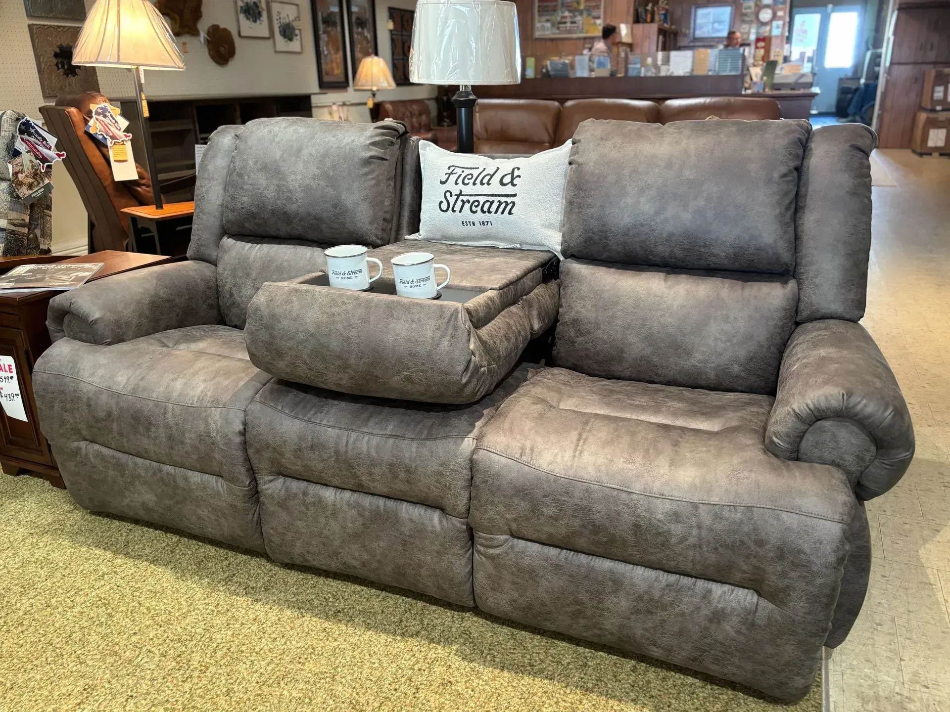 Gray reclining sofa with center console, holding mugs. In a furniture store.