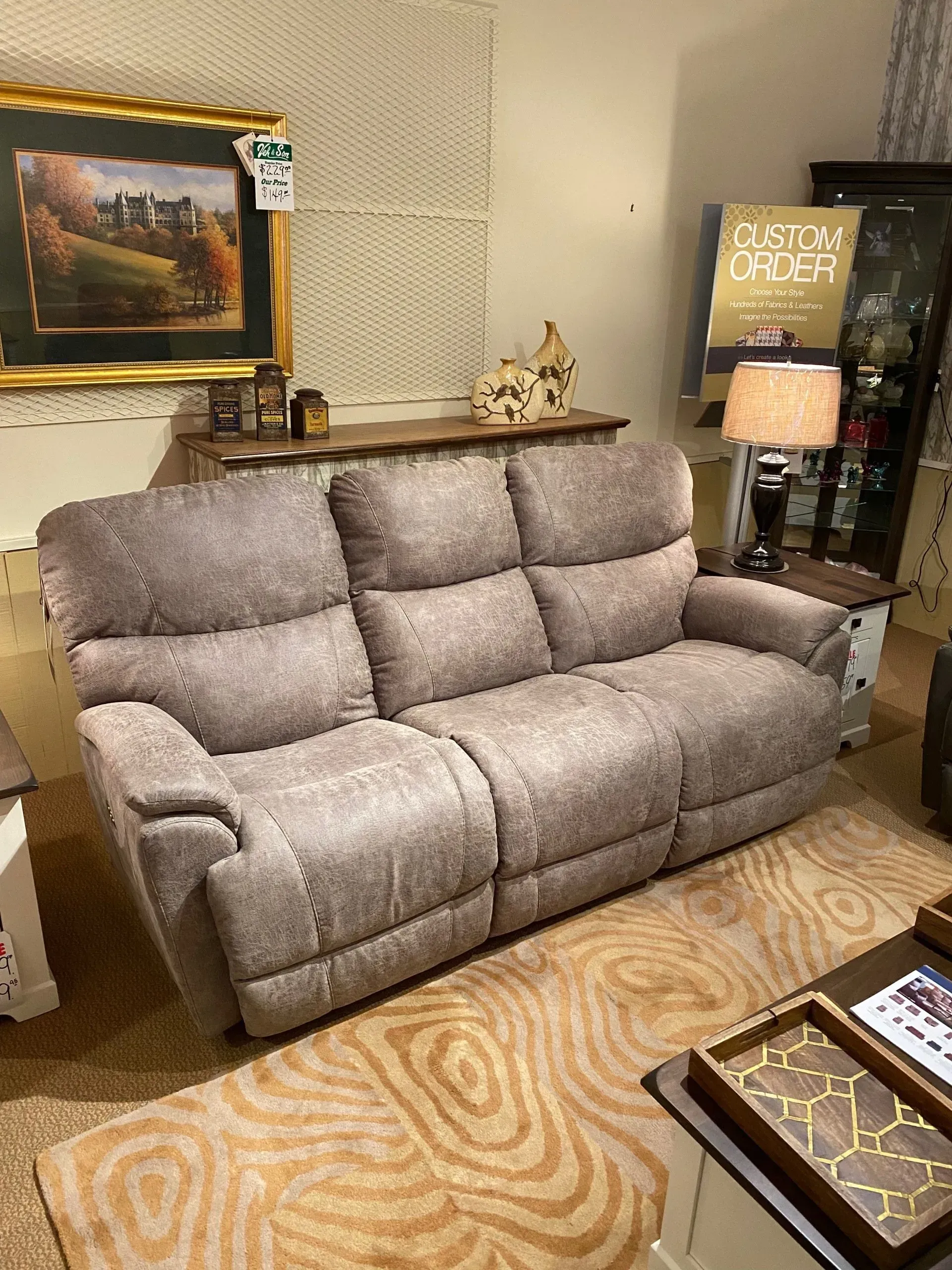 Tan reclining sofa in a room with a painting, side table, and rug.