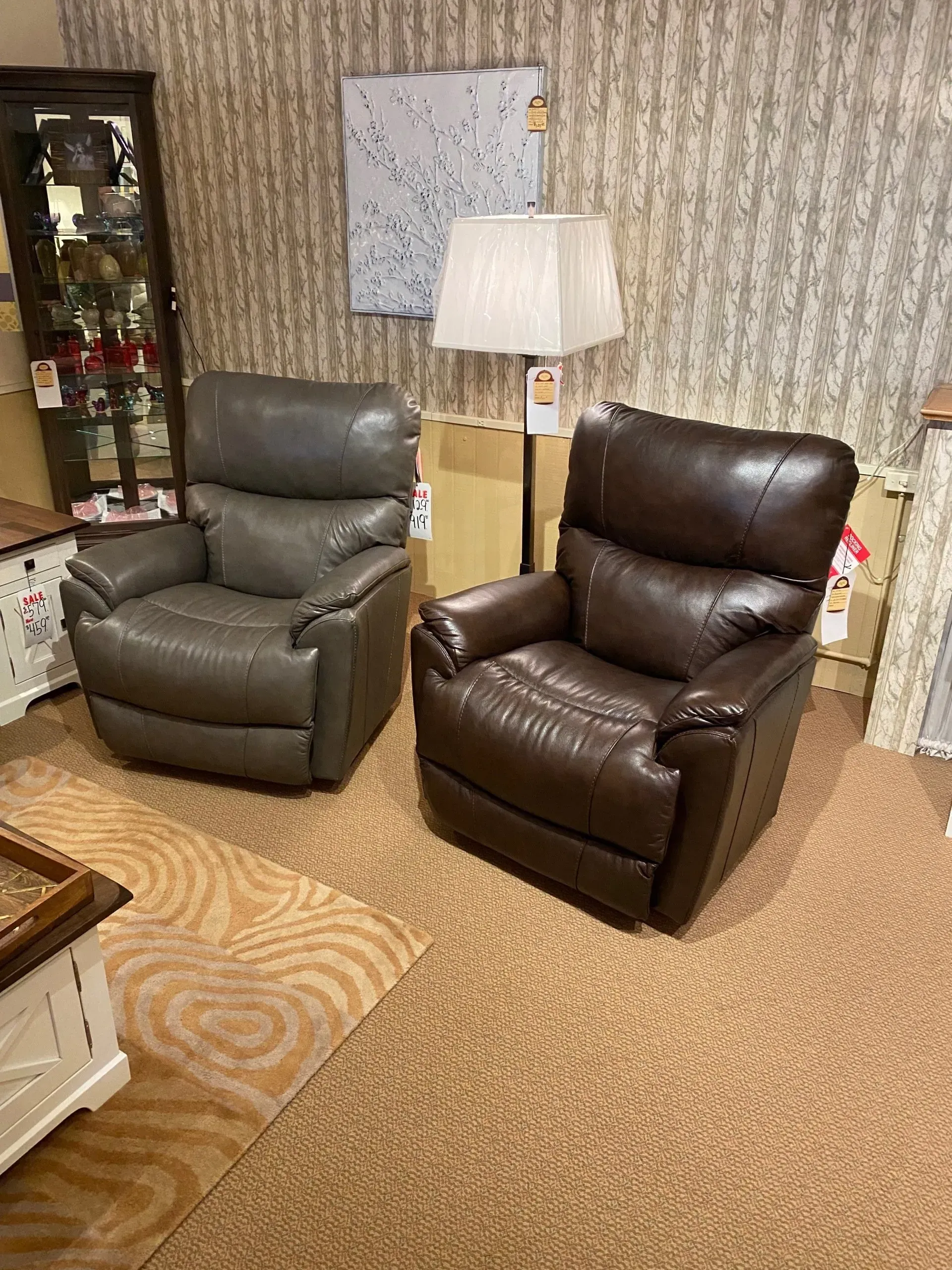 Two leather recliners, gray and brown, sit on a rug in a furniture store.