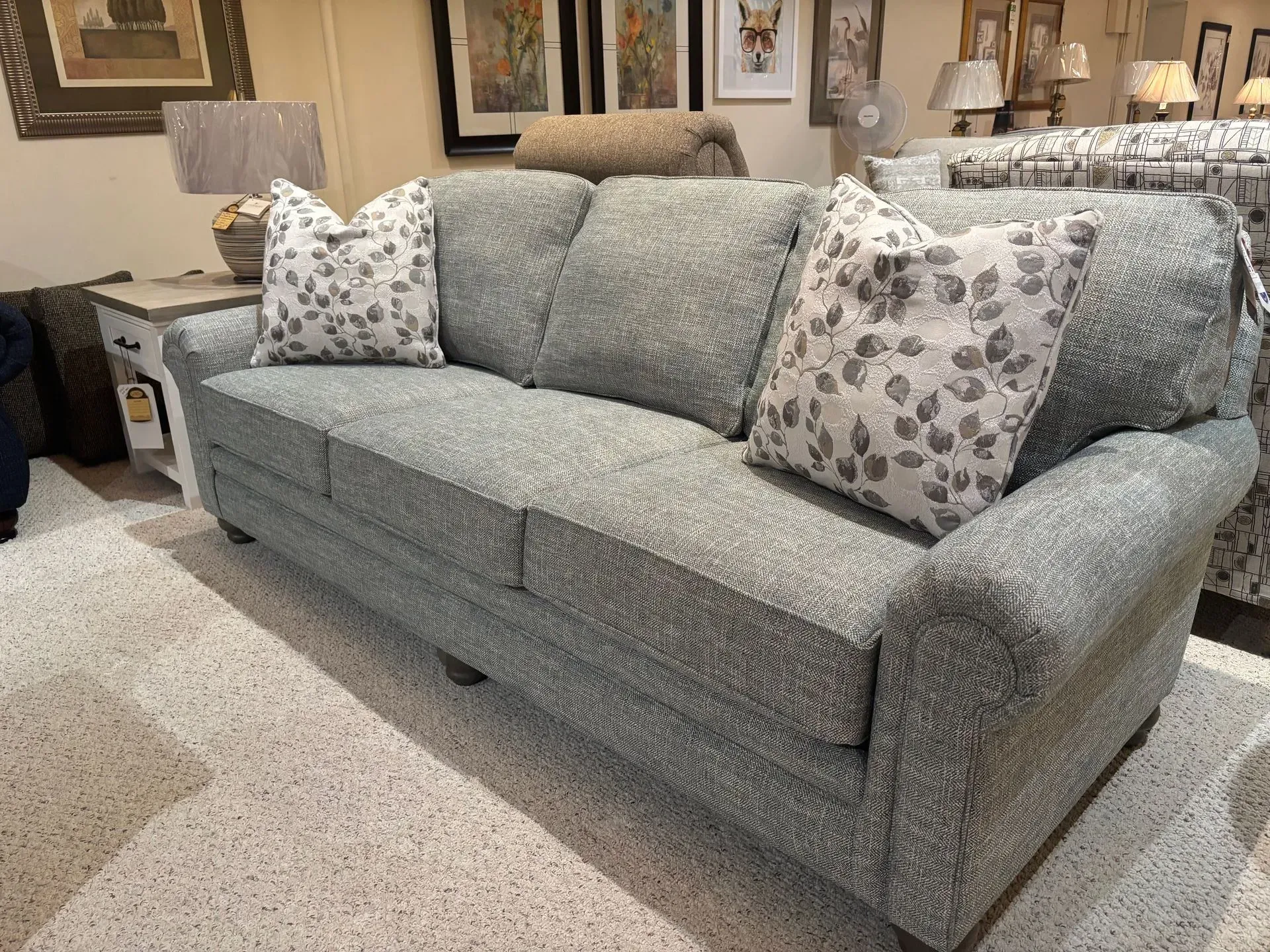 Gray upholstered sofa with floral pillows in a showroom.