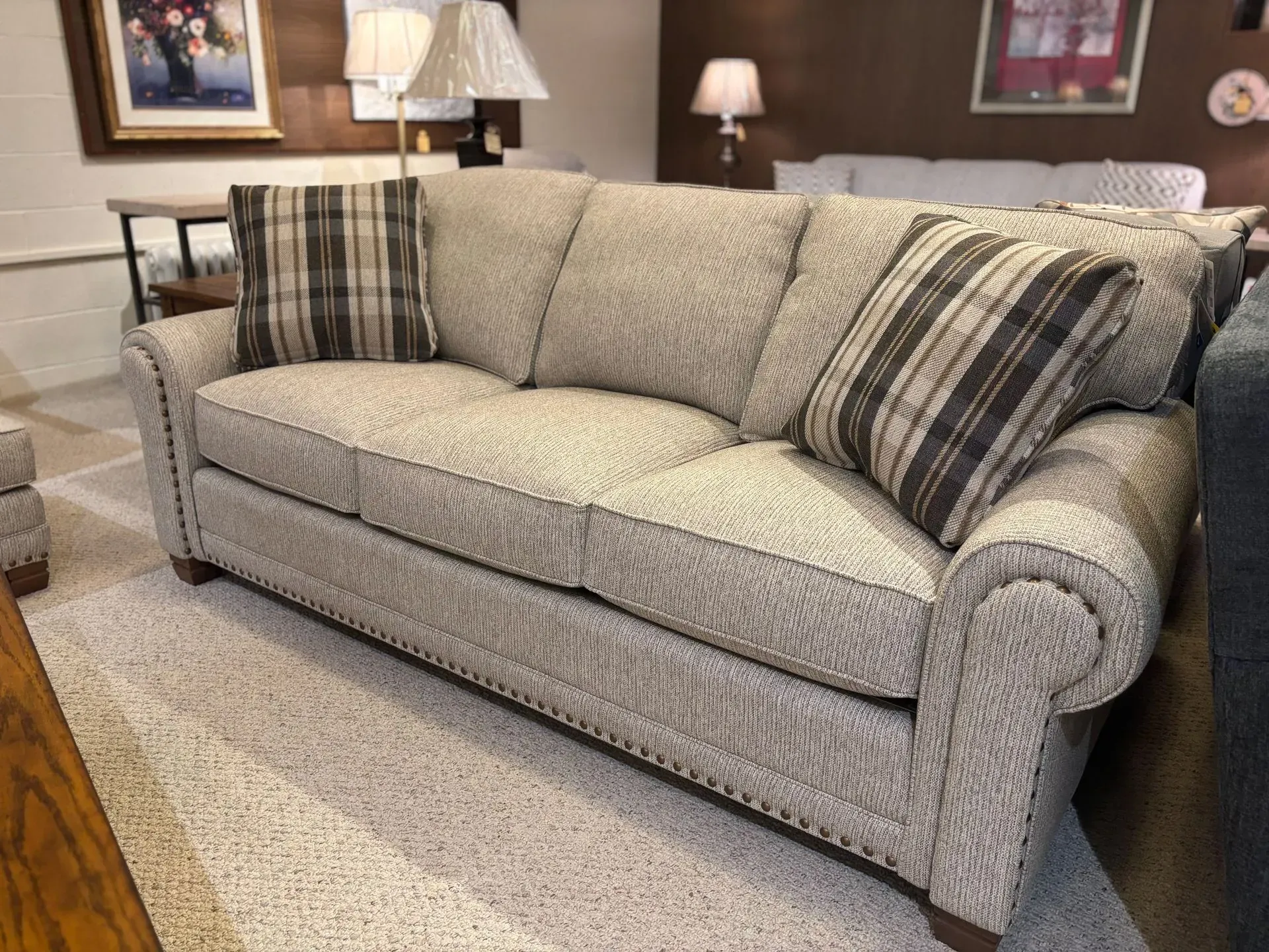 Beige sofa with plaid throw pillows in a showroom setting.