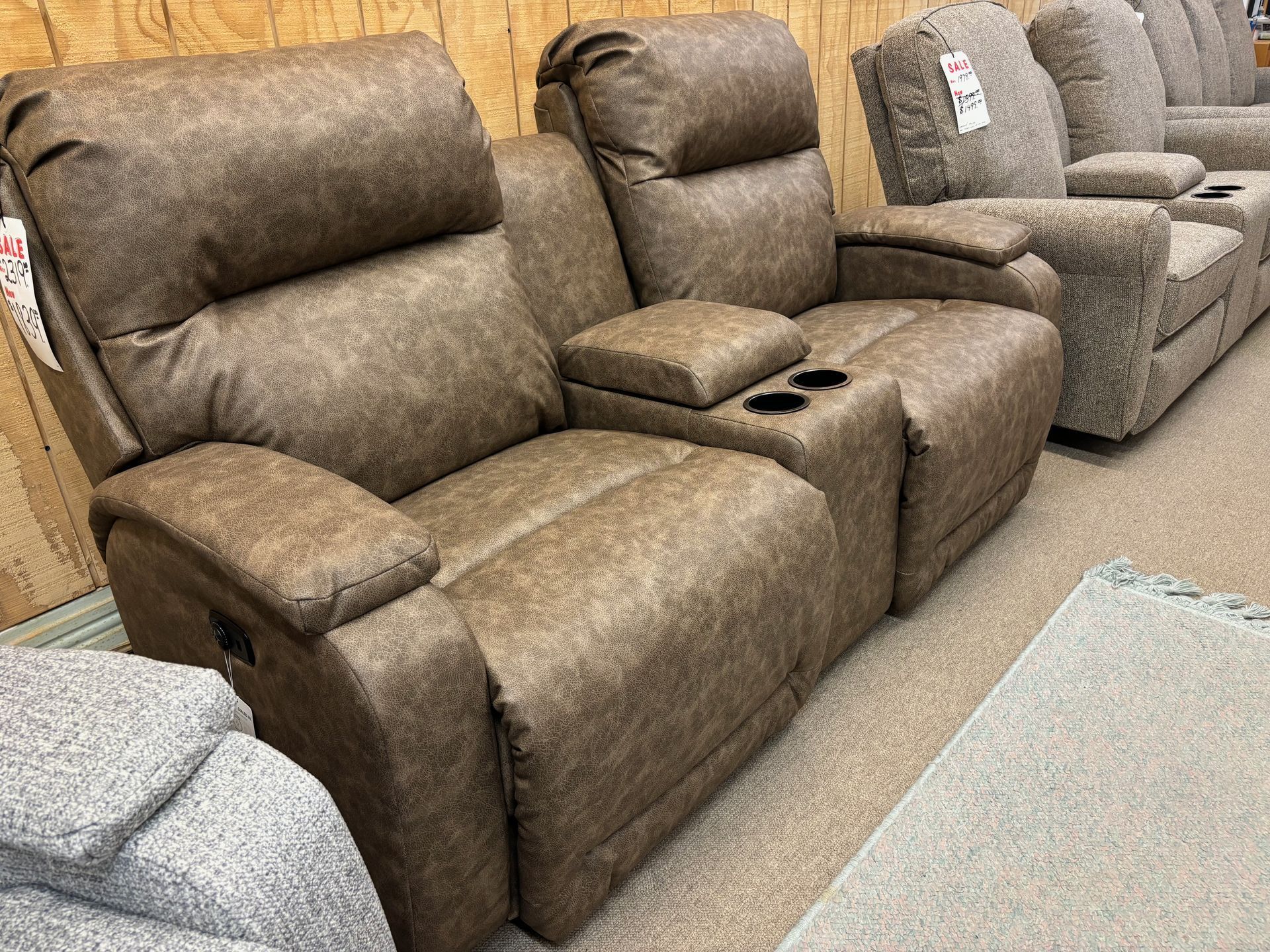 Brown recliner loveseat with center console cup holders, in a furniture store setting.
