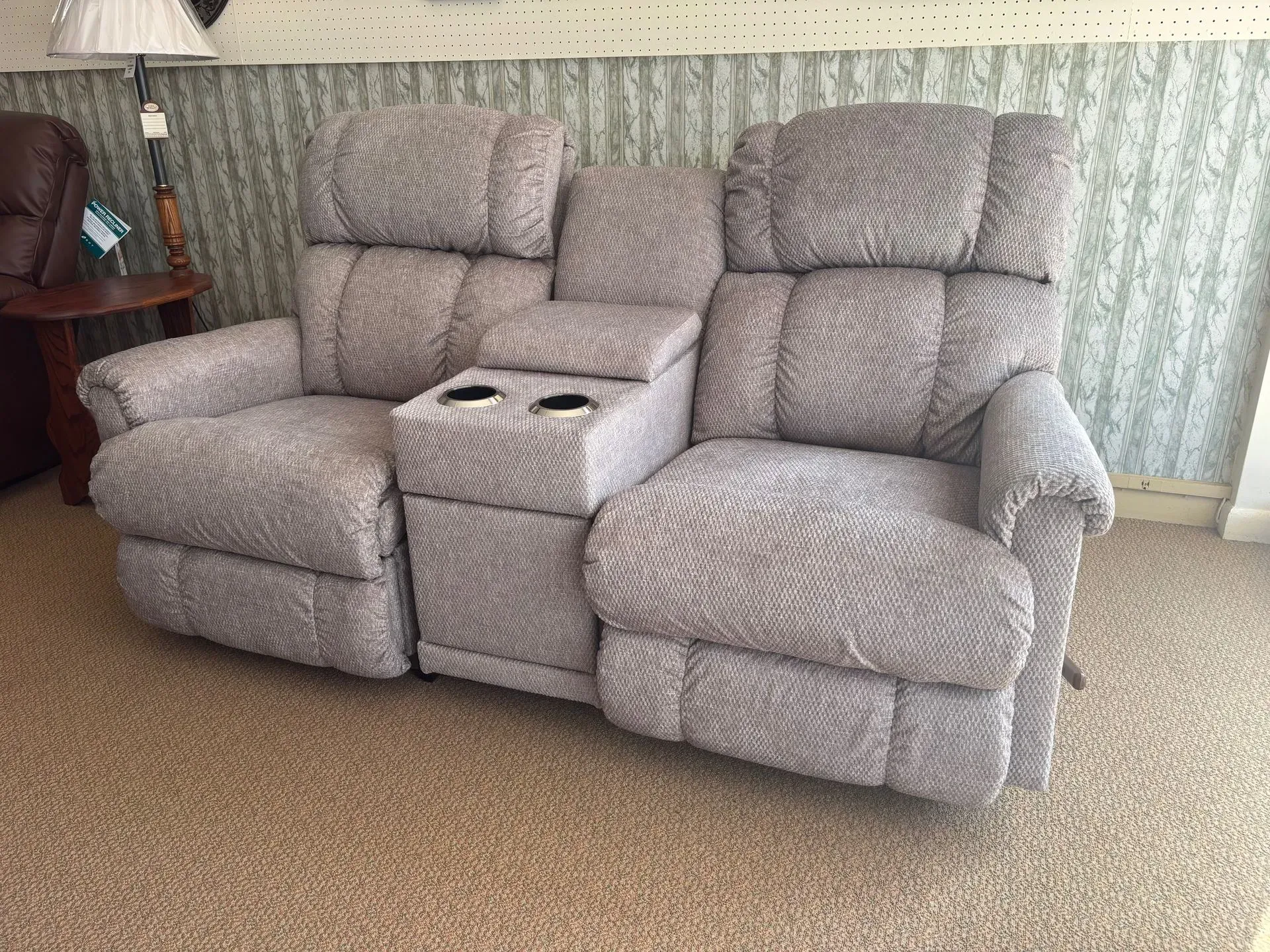 Two-seat gray recliner sofa with console, two cup holders, in a furniture store.