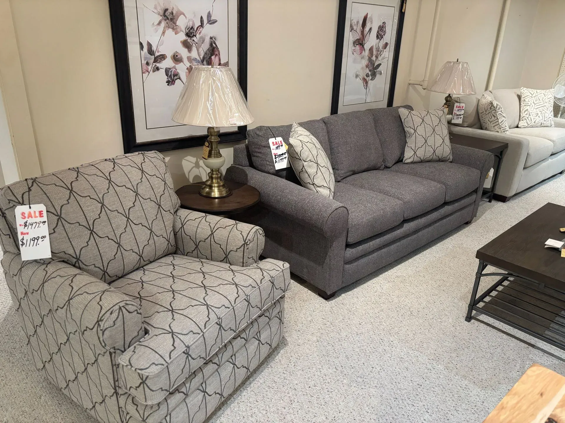 Living room furniture display: patterned armchair, gray loveseat, lamp on table, and additional sofa.