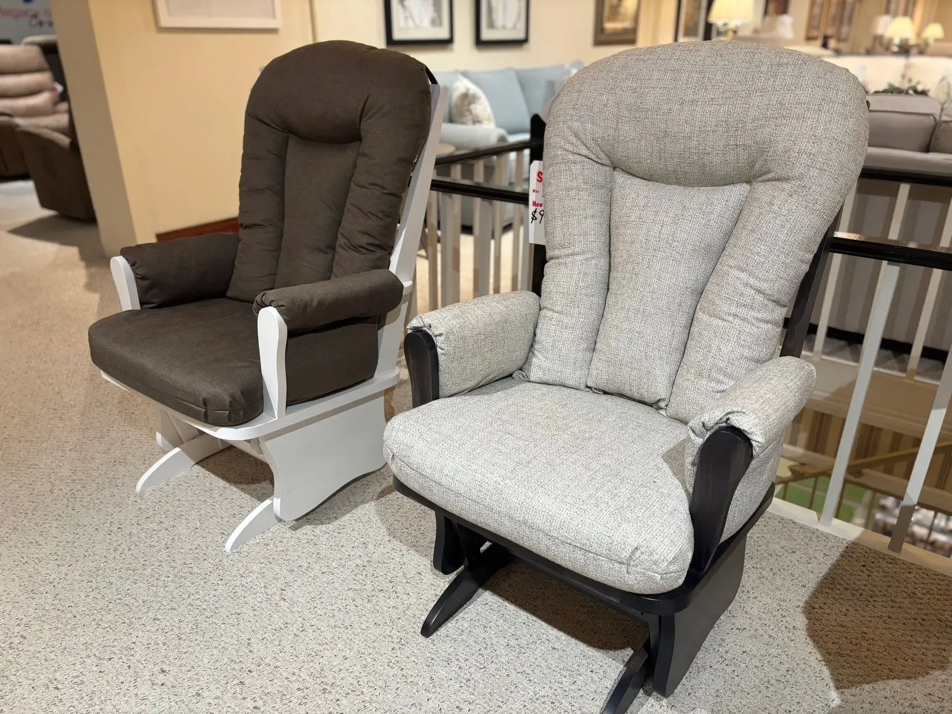Two glider chairs with upholstered backs and arms, one brown and one gray, on a speckled floor.