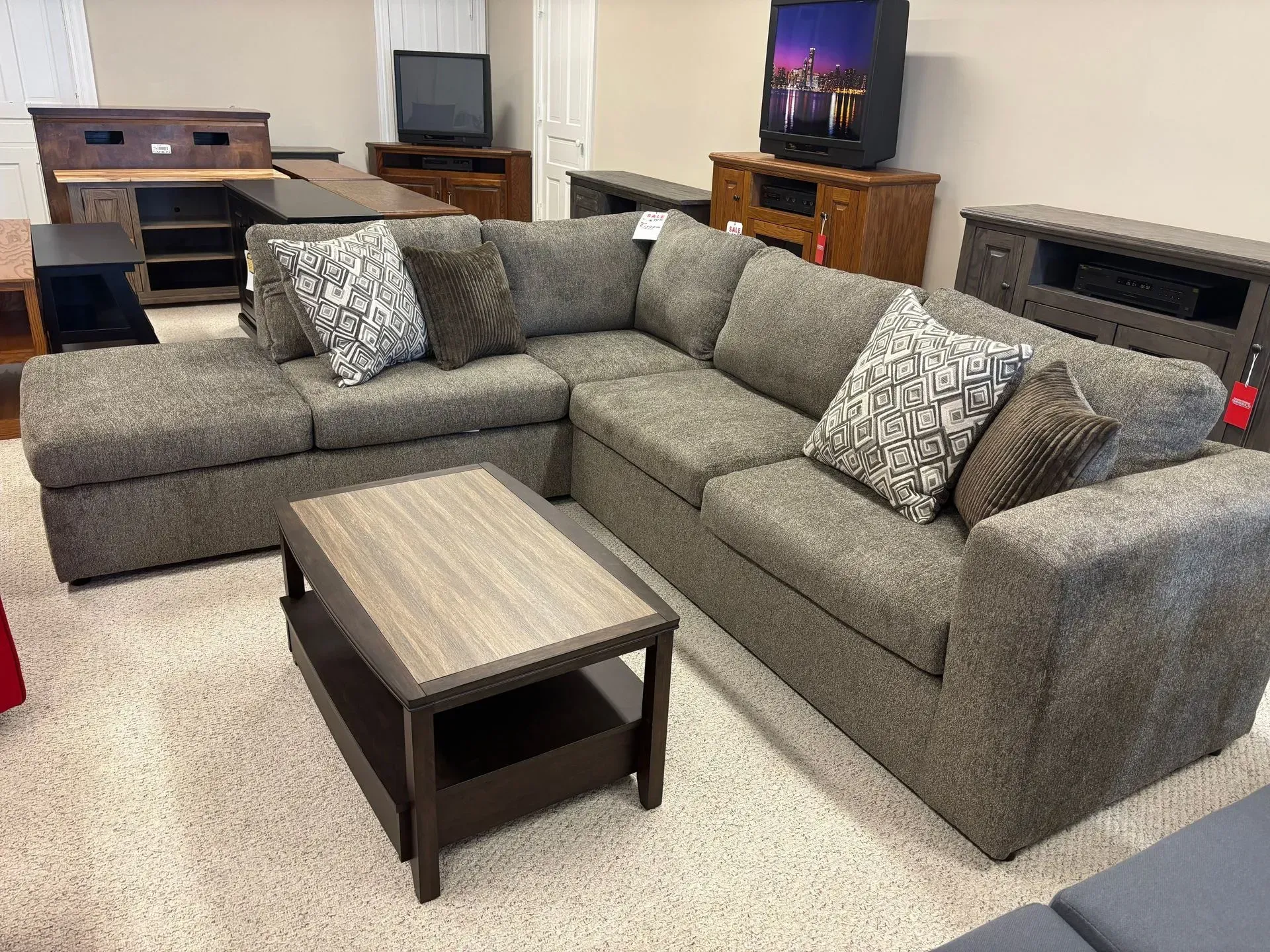 L-shaped gray sectional sofa with accent pillows and a wooden coffee table in a furniture store.