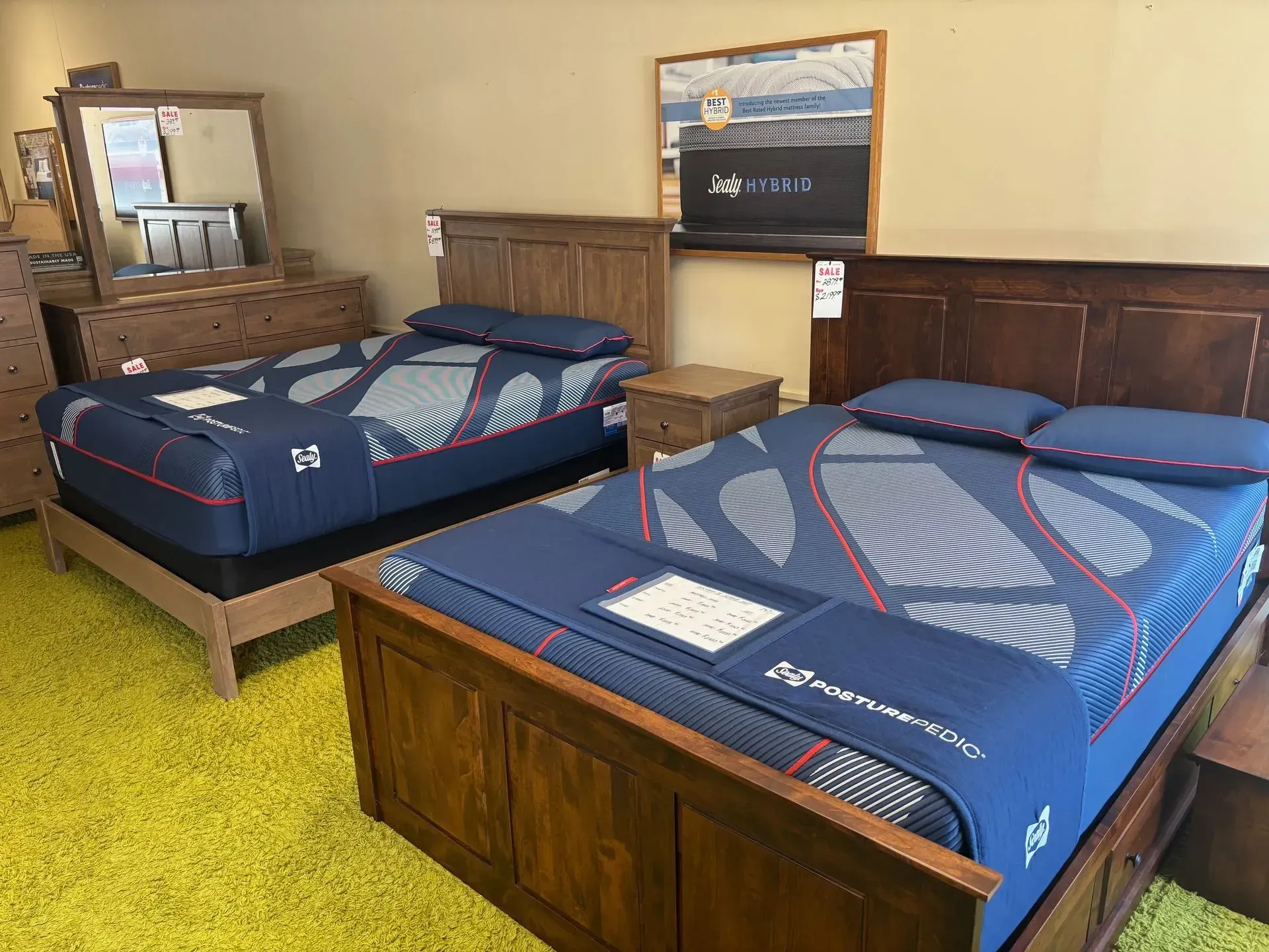 Two wooden beds with blue mattresses in a furniture store, yellow carpet, with bedroom furniture.