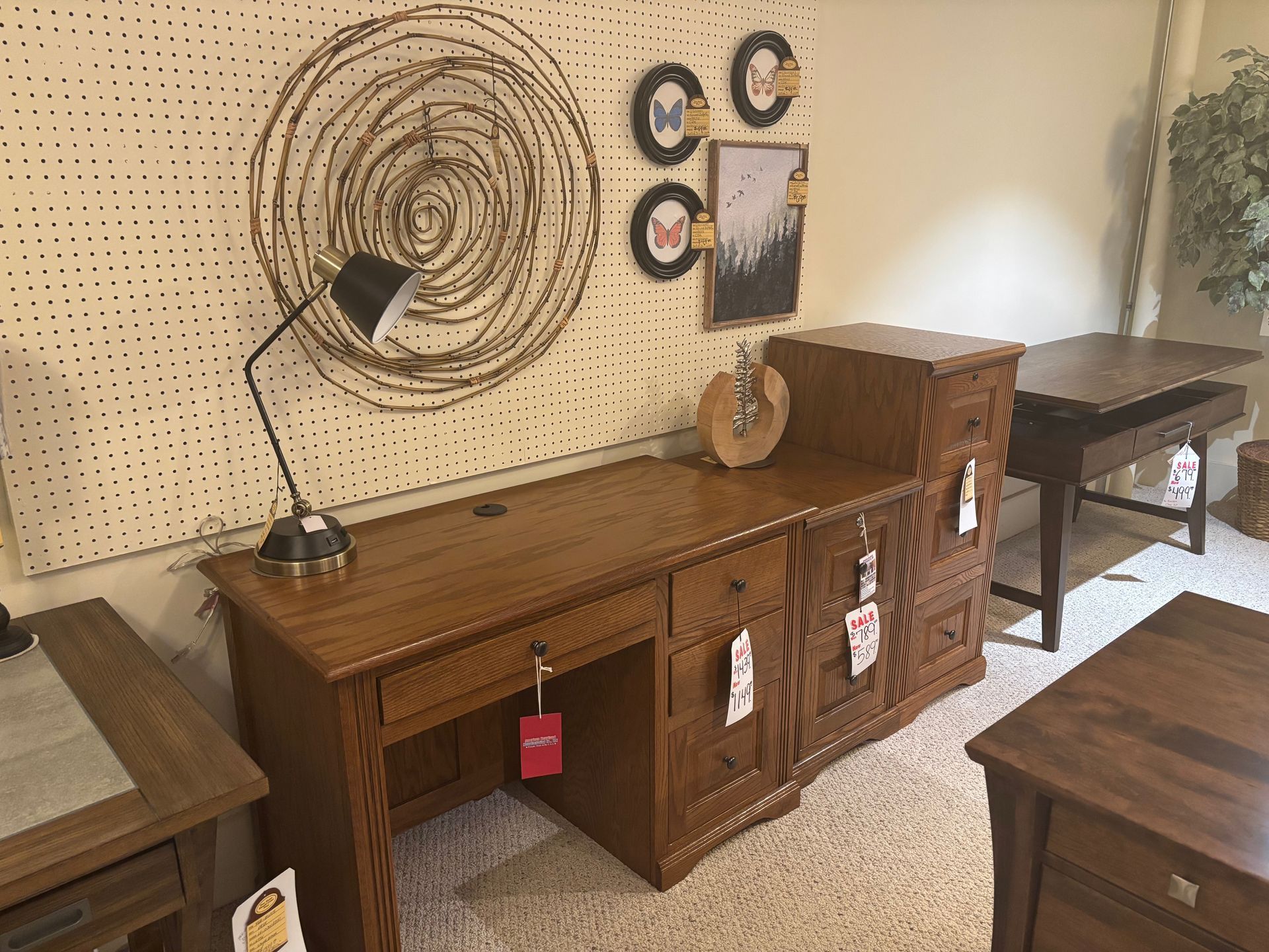 Wooden desk with lamp, art, and furniture display in a showroom setting.