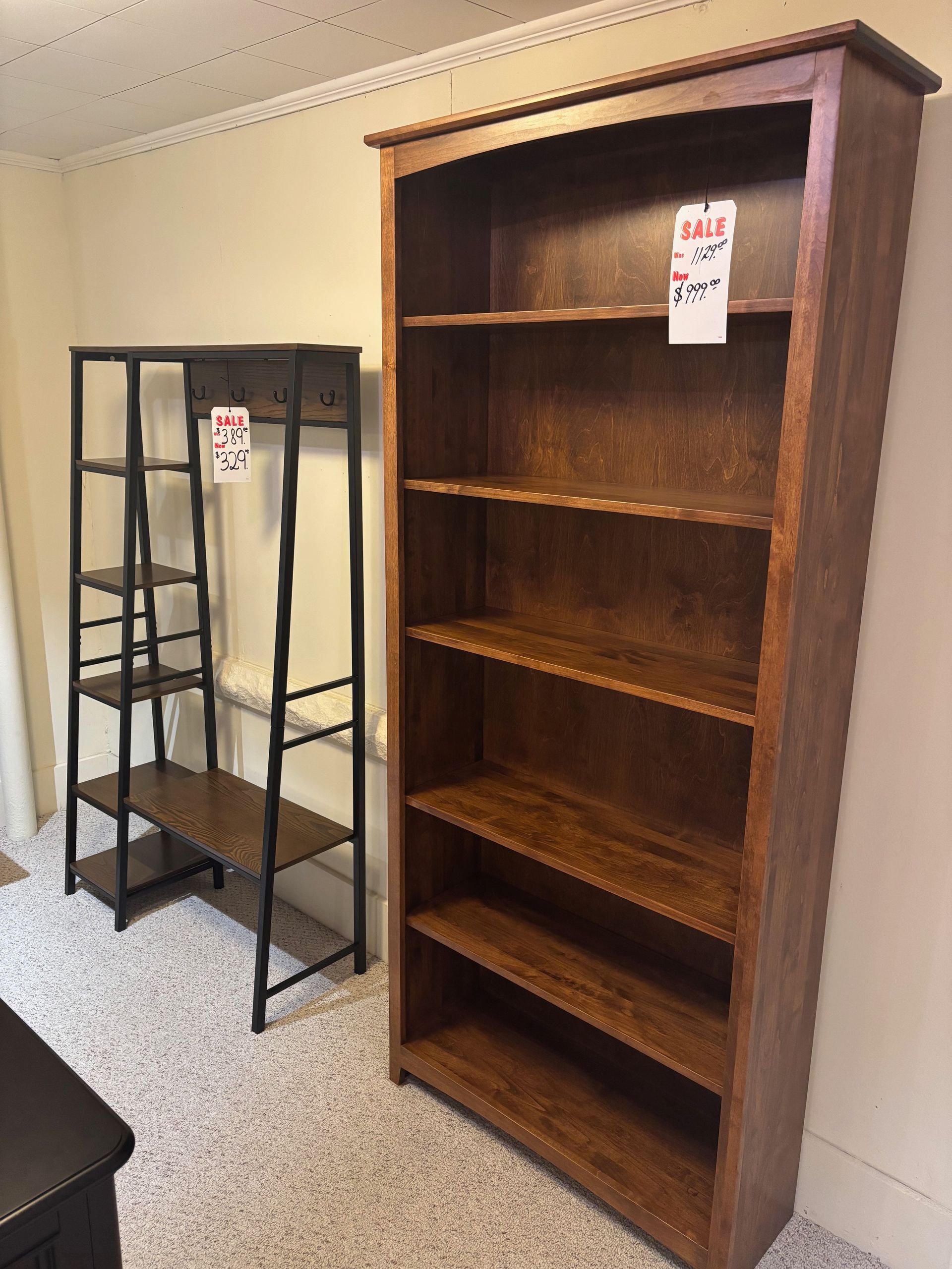 A tall wooden bookshelf next to a black metal shelving unit, both in a room.