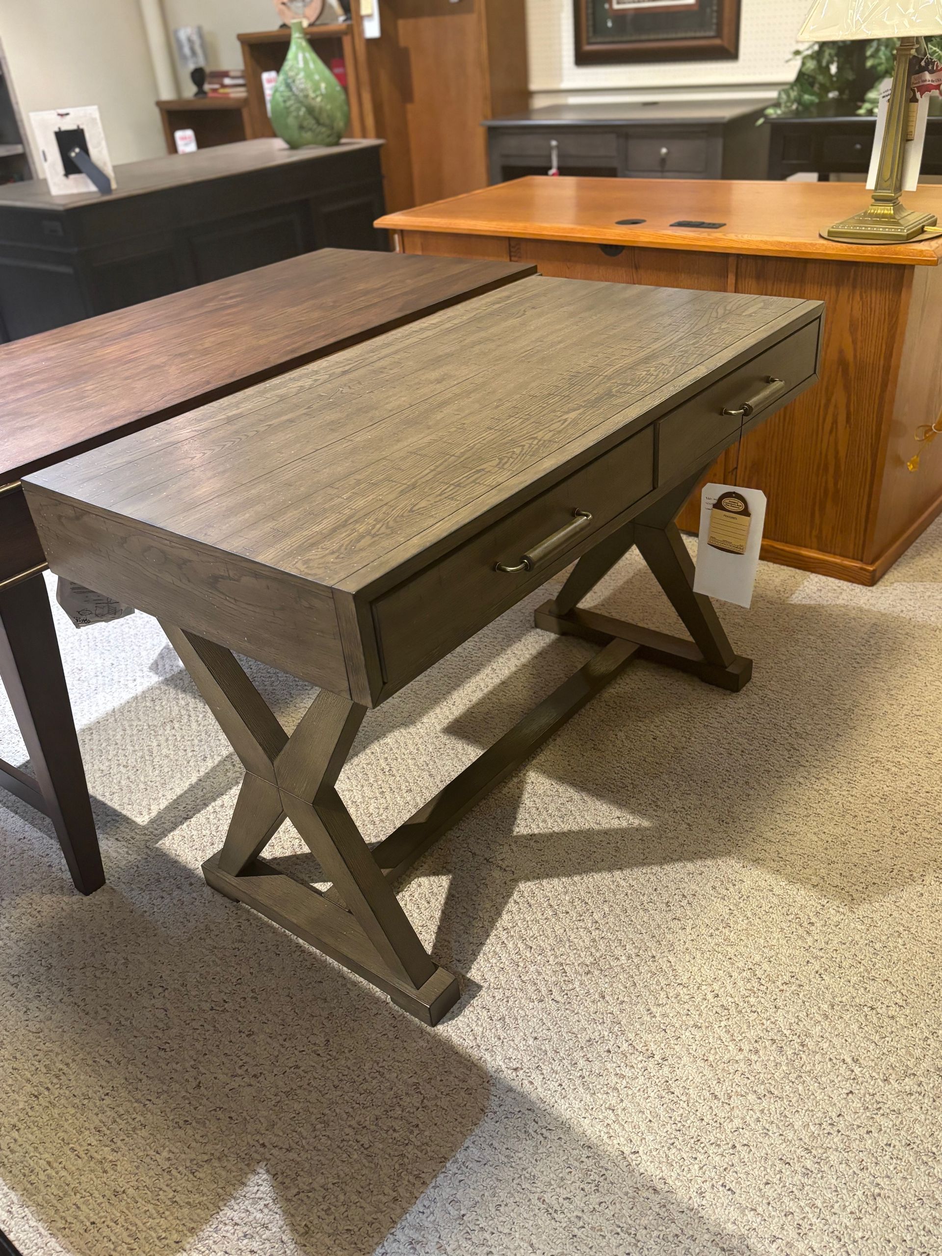 Gray wooden desk with two drawers and X-shaped legs in a furniture store.