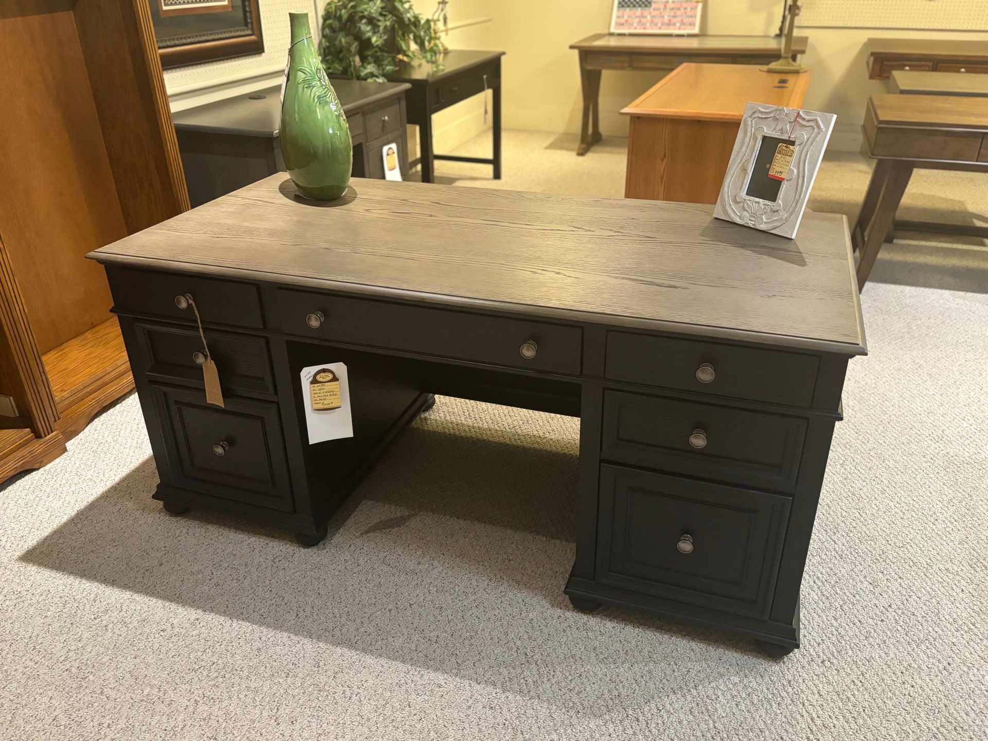 Dark desk with grey top, drawers, green vase, and picture frame in a furniture store.