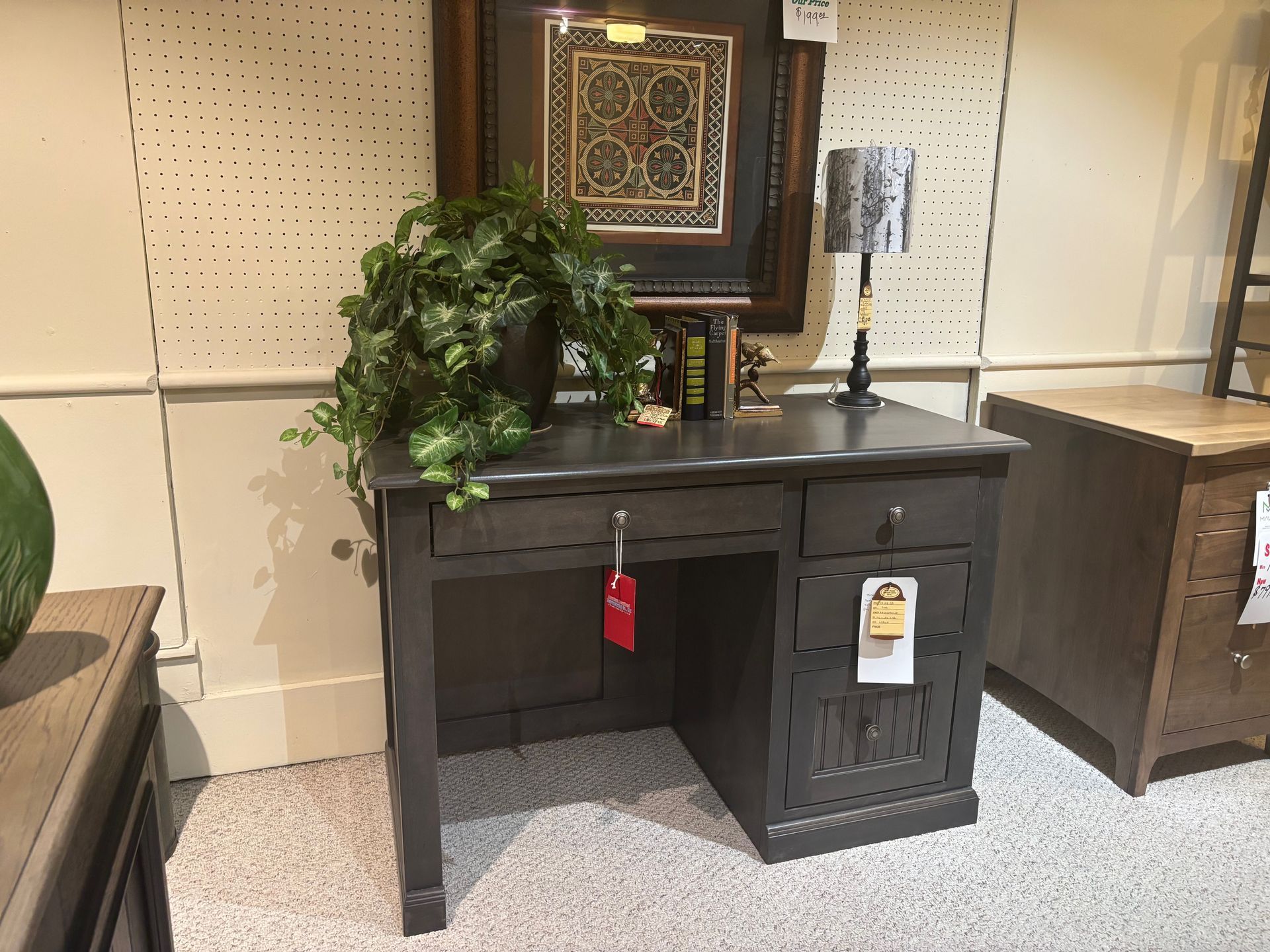 Gray wooden desk with drawers, a plant, and a lamp in a showroom setting.