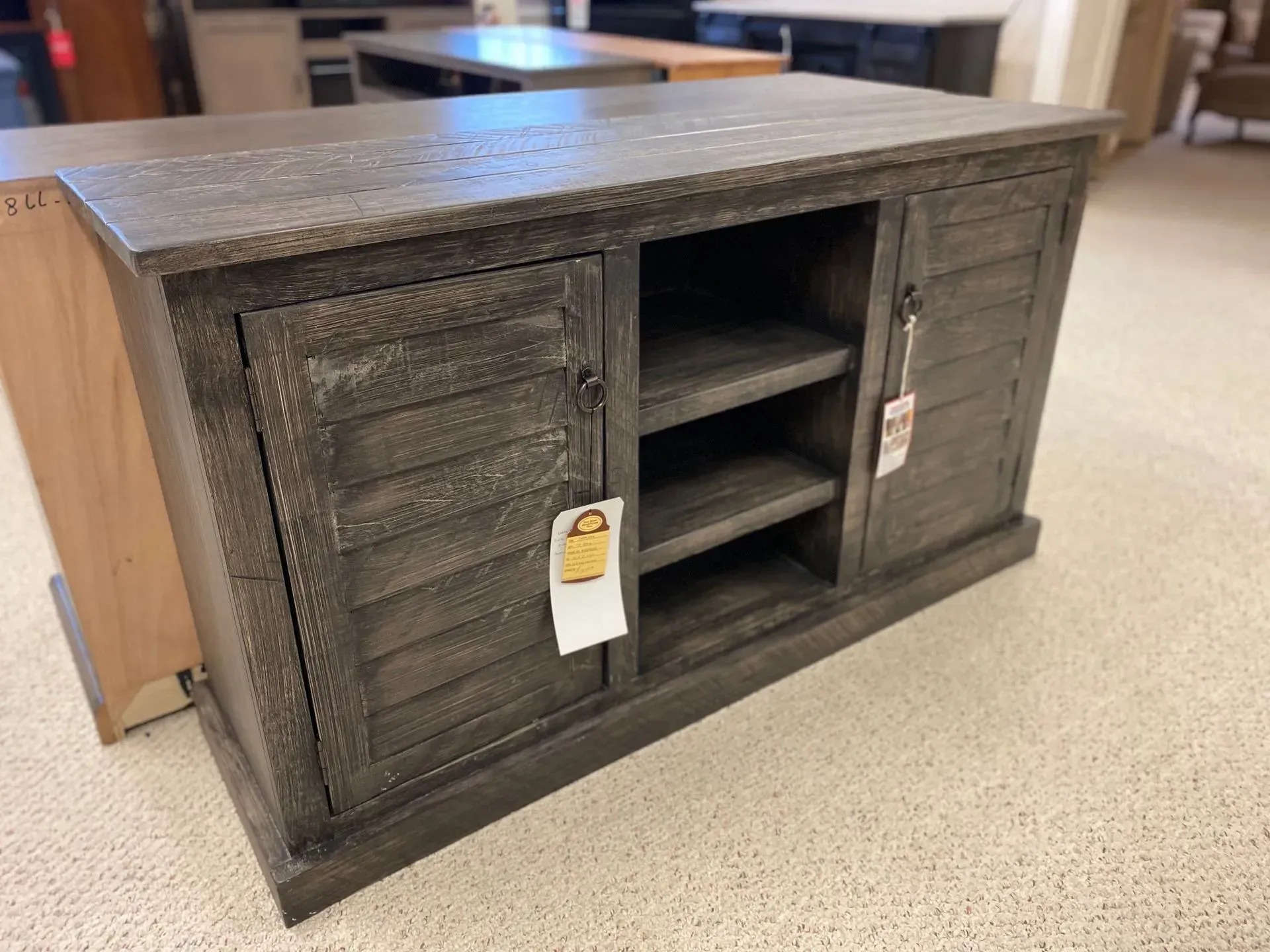 Gray wooden cabinet with shutter-style doors and open shelving, in a store setting.