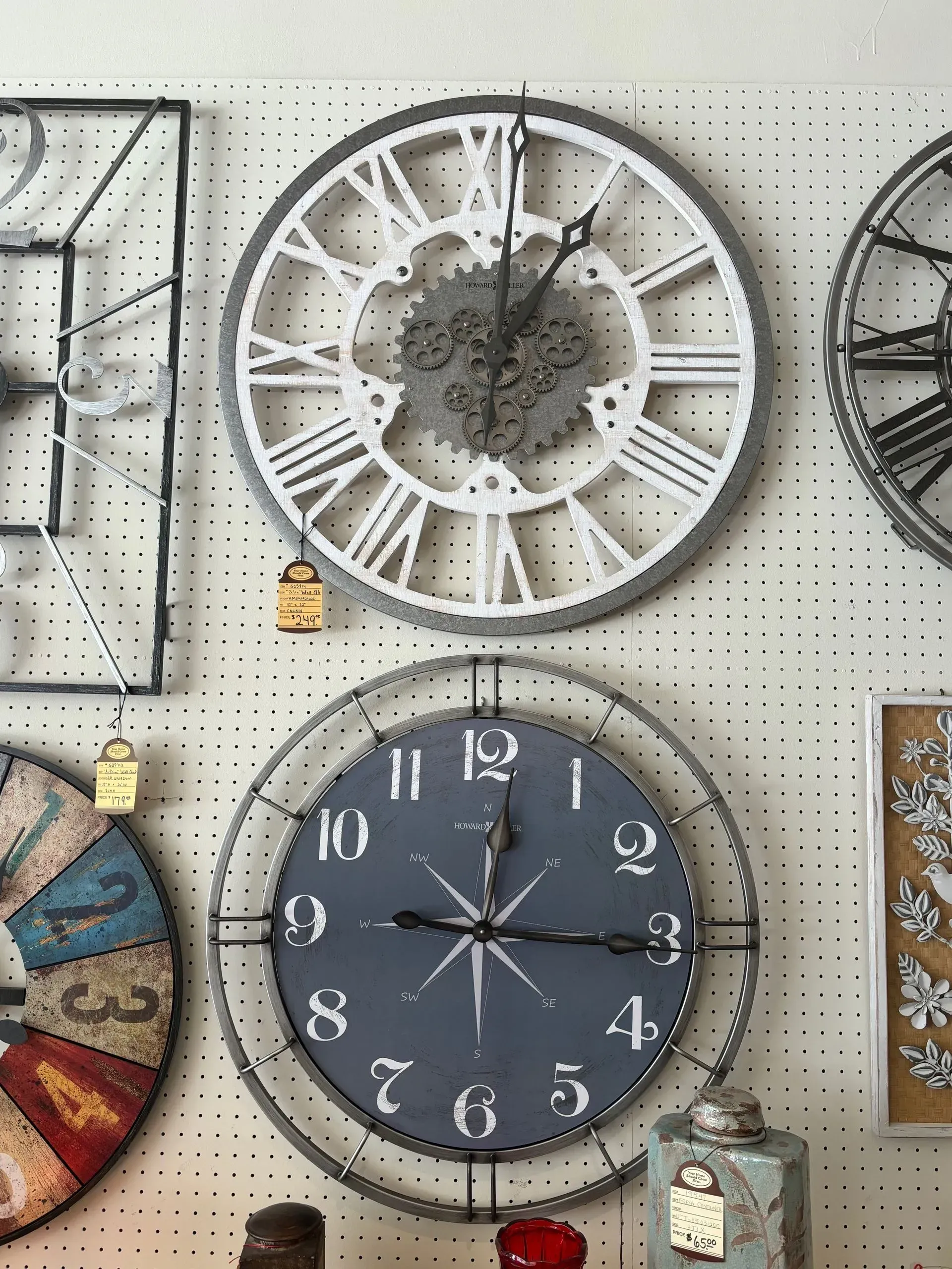 Clocks displayed on a wall. One white, Roman numeral clock; one dark clock with a compass design.