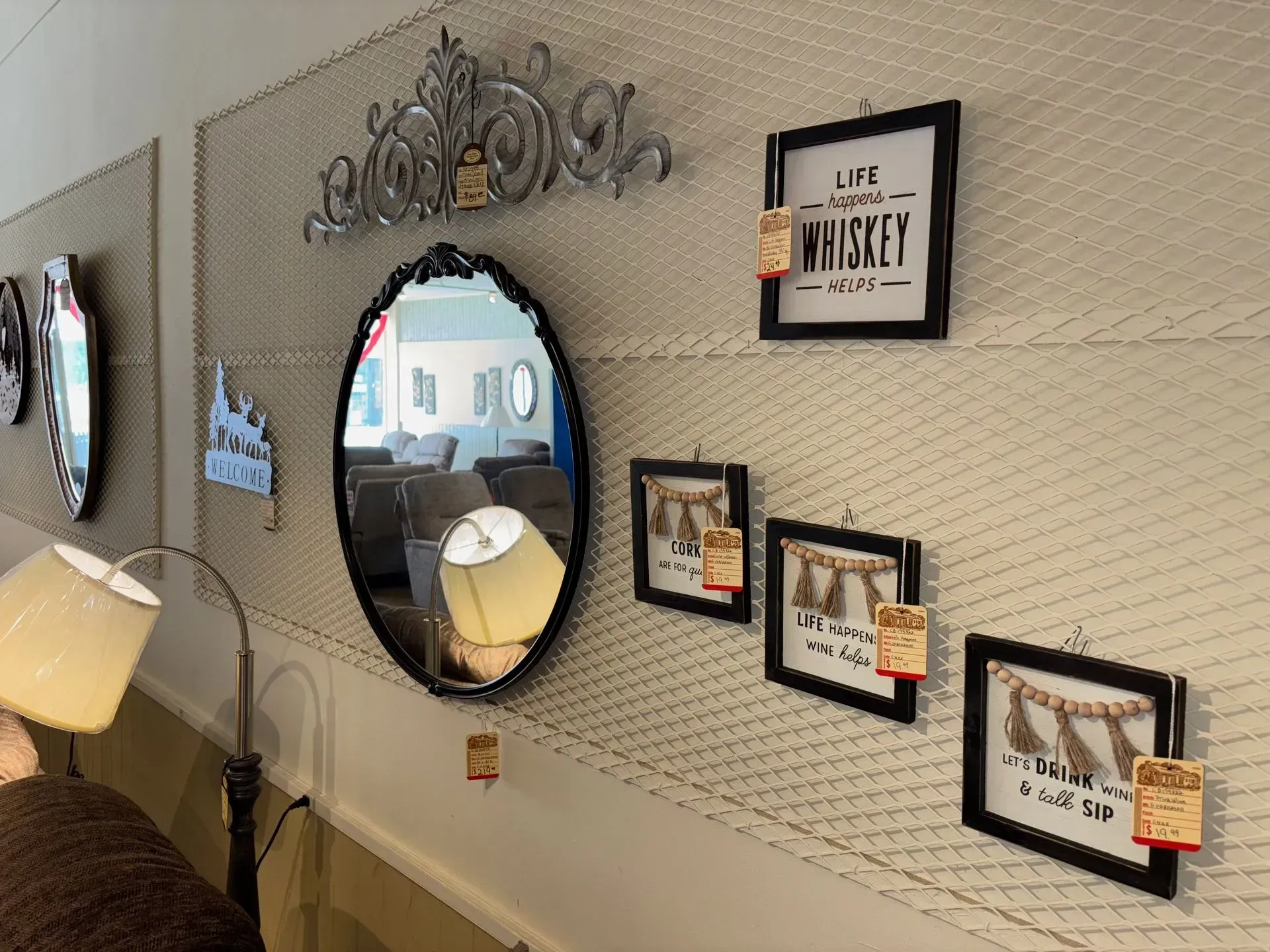 A retail wall display with mirrors, framed art, and decorative metalwork against a beige grid backdrop.